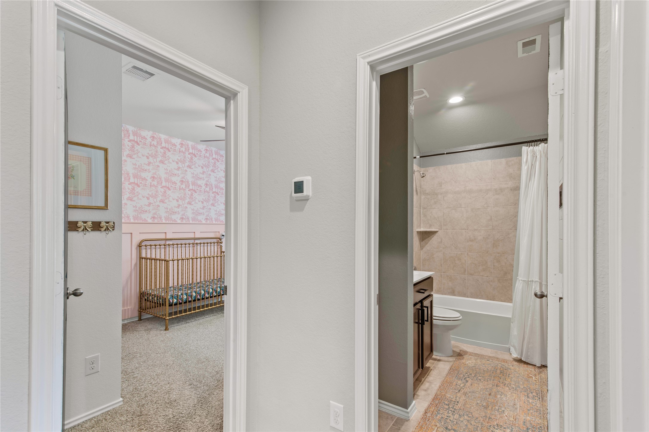 Charming hallway leads to a cozy nursery with pink wallpaper and a sleek bathroom featuring a modern tub and shower.