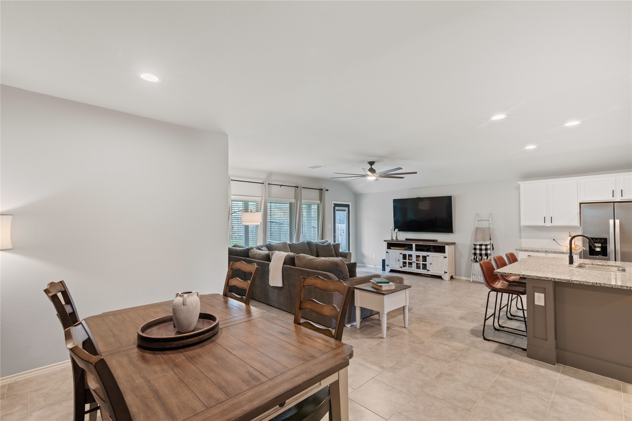 Spacious open-concept living area featuring a cozy seating arrangement, a large wall-mounted TV, and a modern kitchen with a breakfast bar.