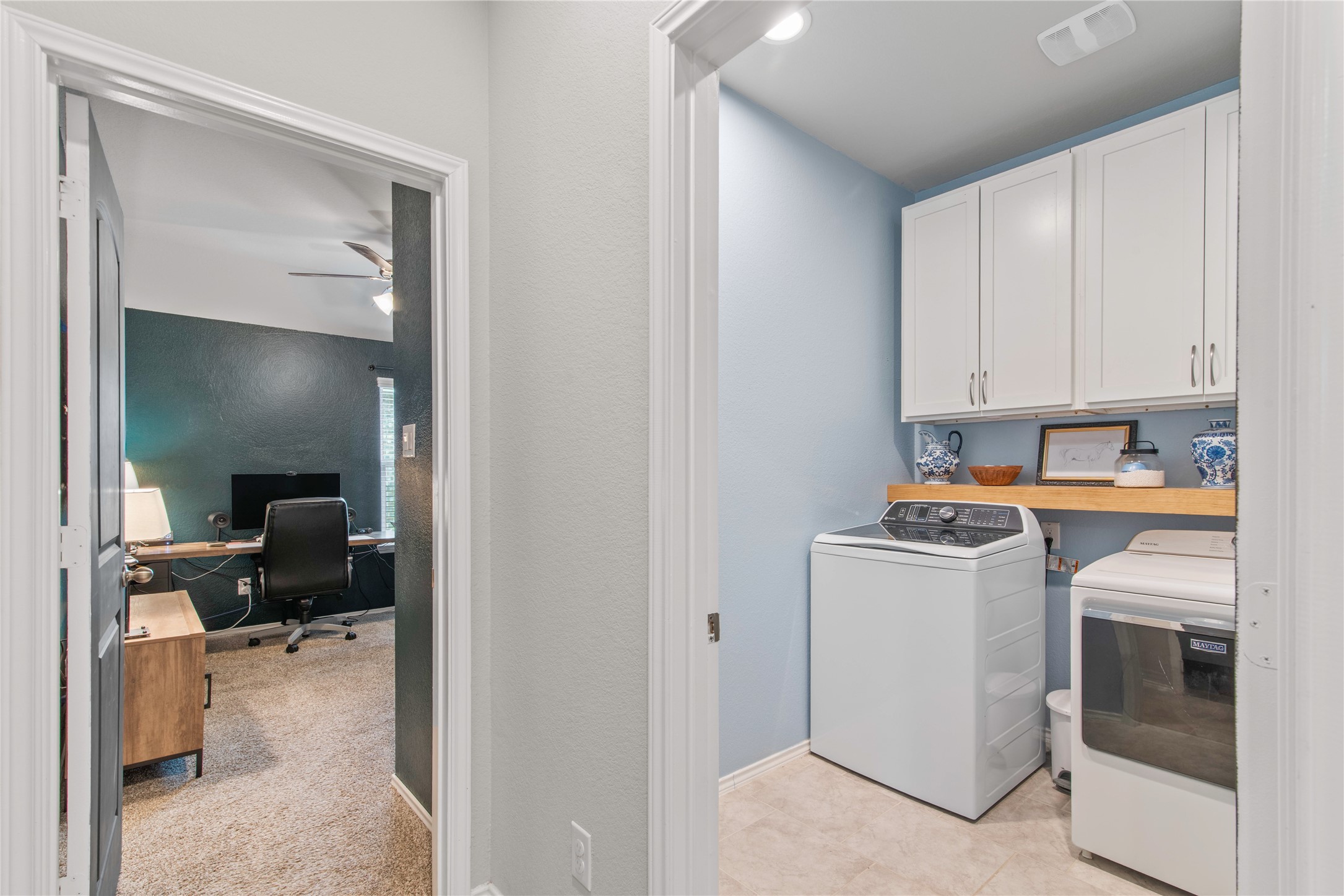 Conveniently designed laundry room with ample cabinetry and modern appliances, adjacent to a cozy home office space perfect for productivity.