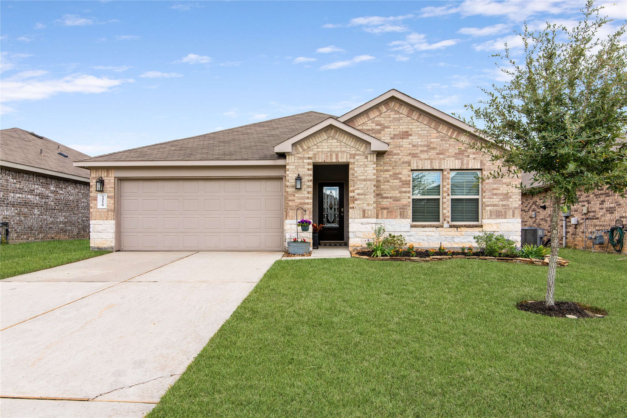 Charming brick home with a spacious two-car garage, manicured lawn, and inviting front entry.