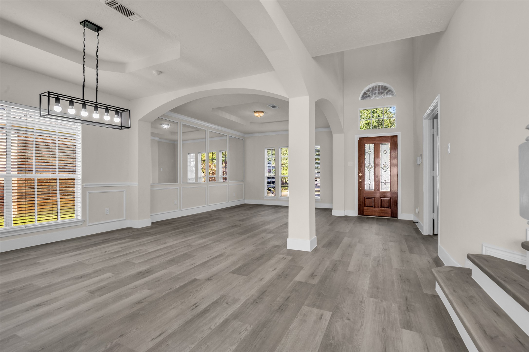 Elegant entryway with high ceilings, modern light fixtures, and abundant natural light, featuring stylish wood flooring and classic architectural detailing.