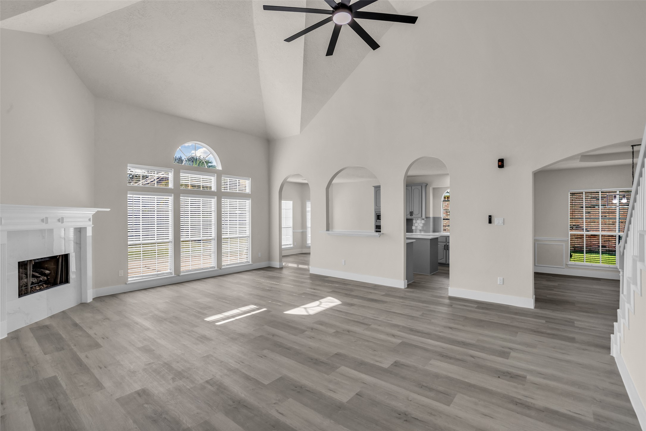 Spacious living area with high vaulted ceilings, abundant natural light from large windows, and elegant archways leading to a modern kitchen.