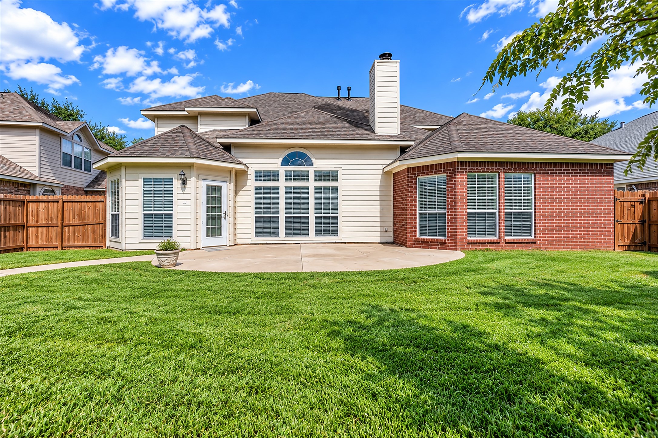 Charming backyard with a spacious patio, lush green lawn, and a blend of brick and siding exterior, offering privacy and a perfect setting for outdoor gatherings.