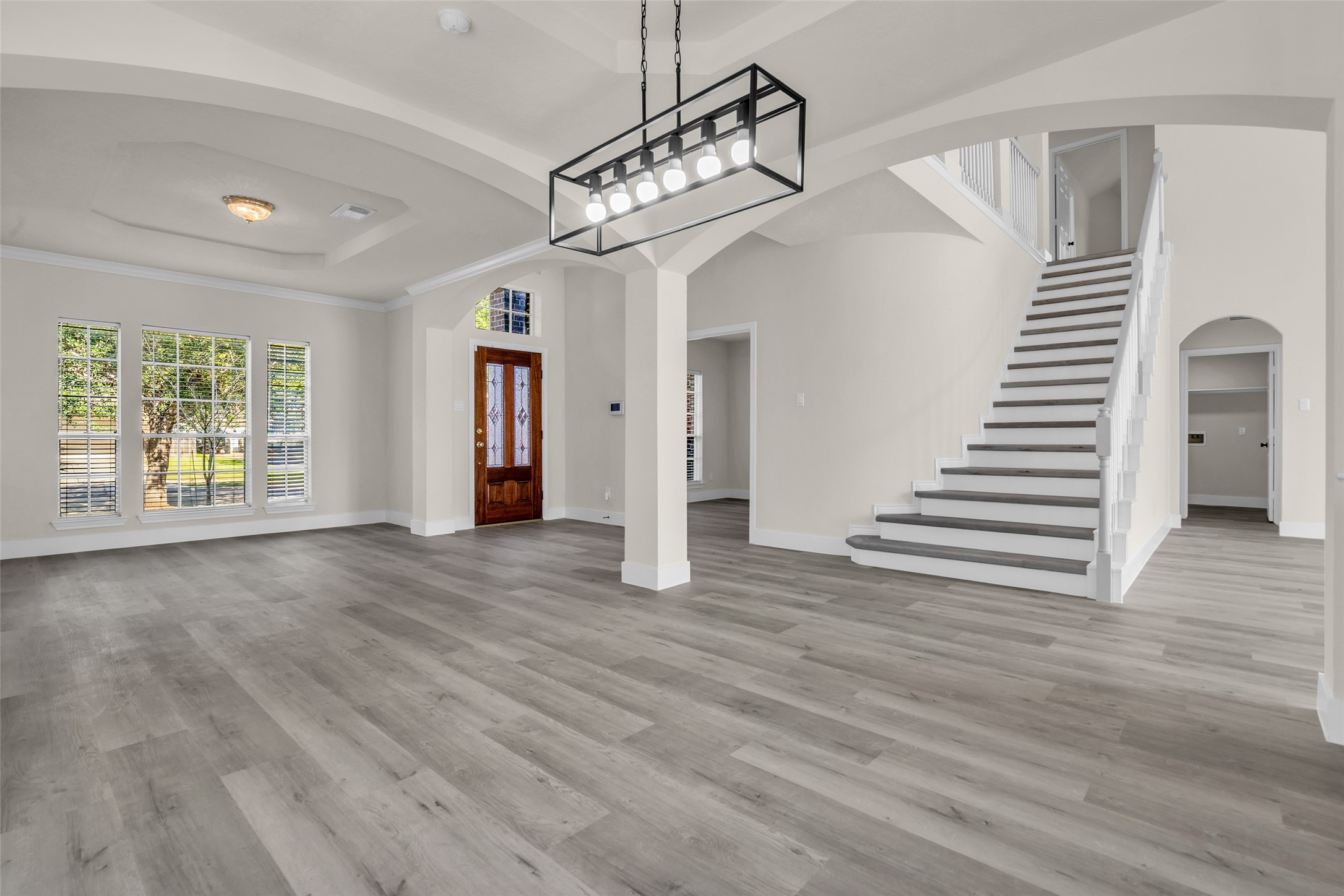 Spacious open-plan dining room with elegant hardwood floors and abundant natural light features a grand staircase leading to the upper level.