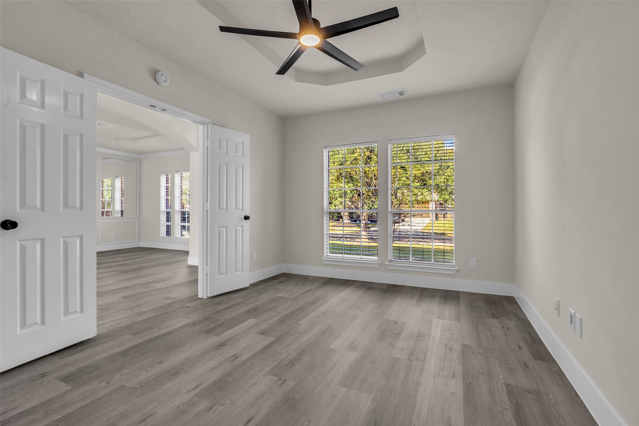 Den/study area with large windows, modern ceiling fan, and elegant double doors.