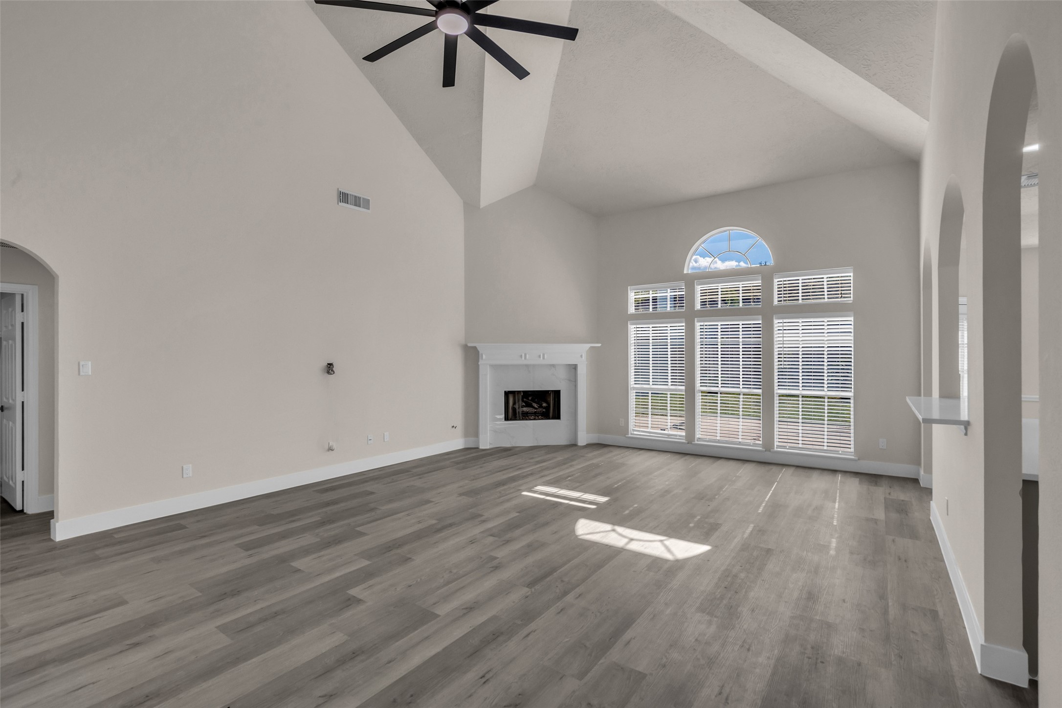 Spacious living area with high ceilings, elegant arched windows, and a cozy fireplace, complemented by sleek wood flooring and modern finishes.