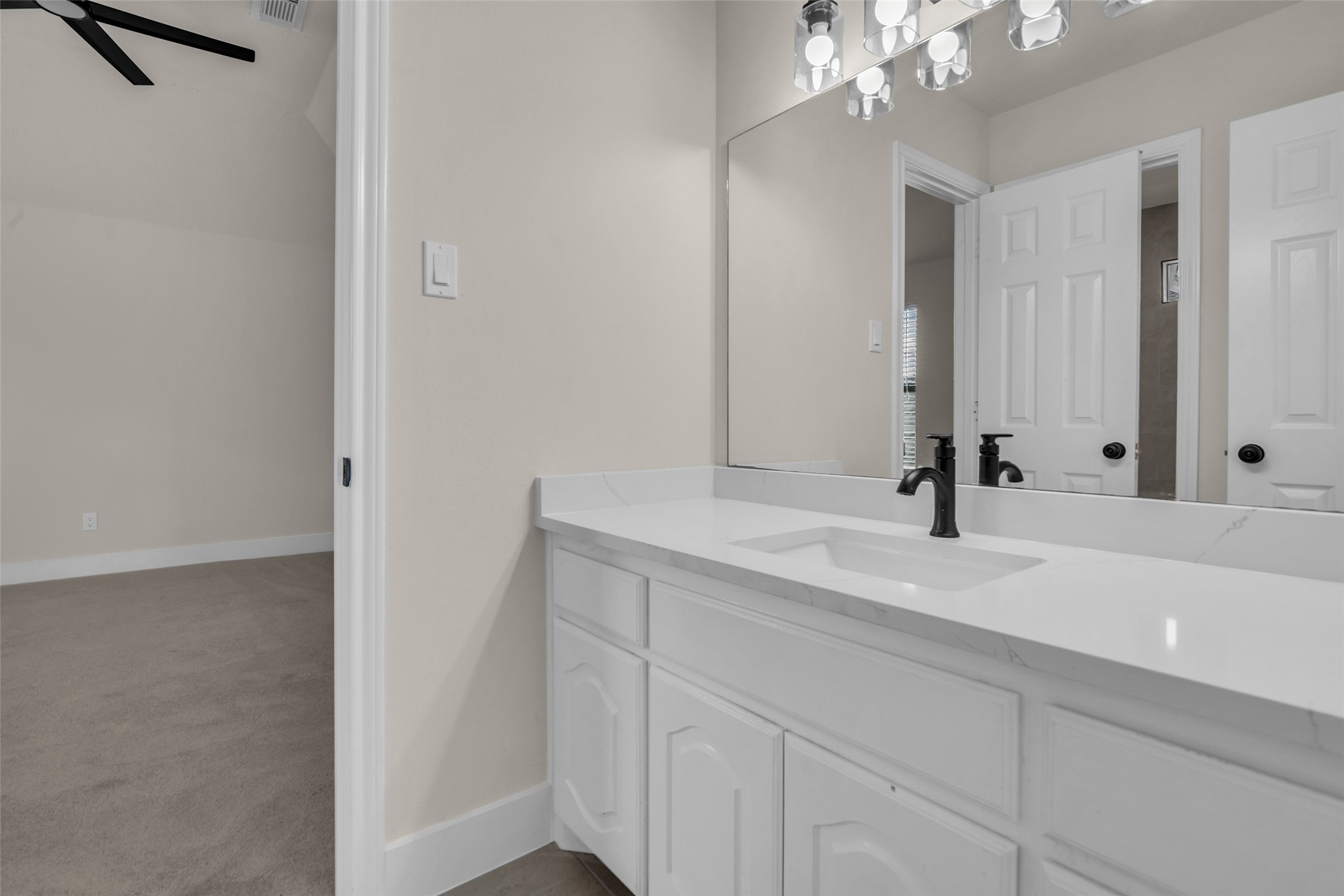 Secondary bathroom with sleek white cabinetry, a spacious countertop, and a large mirror, offering a clean and elegant look.