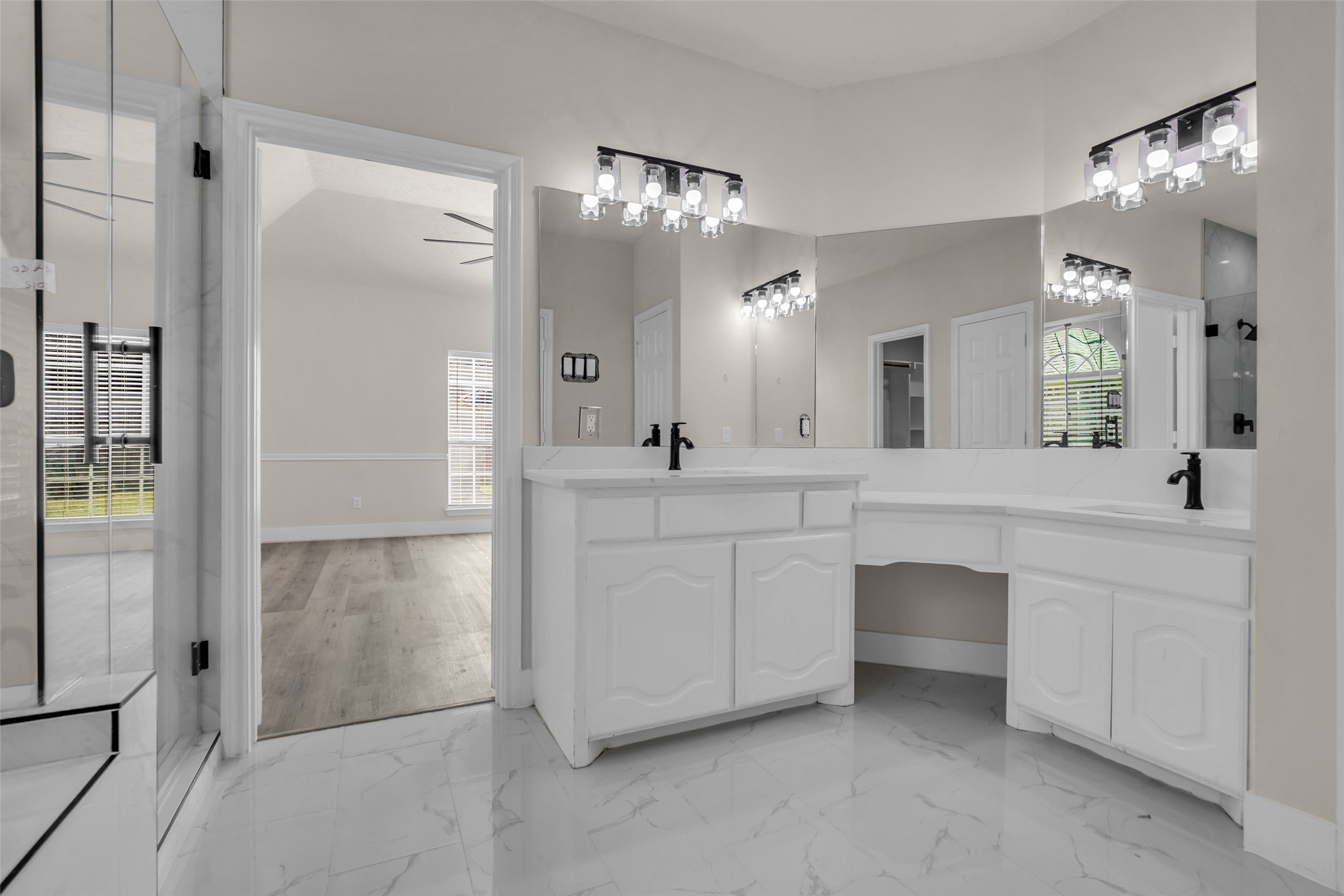Elegant bathroom featuring dual vanities with modern fixtures, ample counter space, and stylish lighting, seamlessly flowing into a bright room with rich wood flooring.
