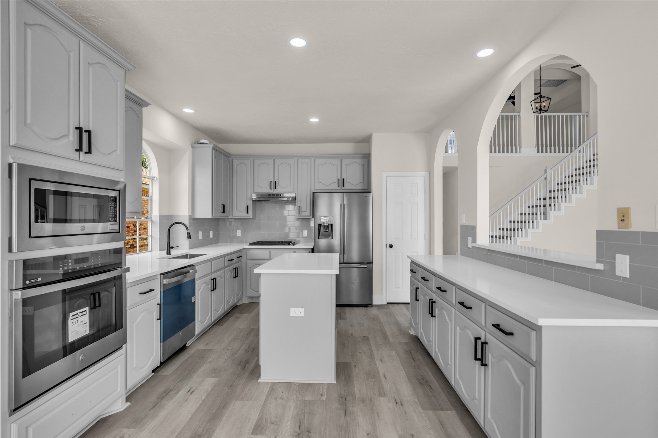 Modern kitchen featuring sleek gray cabinetry, stainless steel appliances, and a spacious island, complemented by stylish arched entries and abundant natural light.