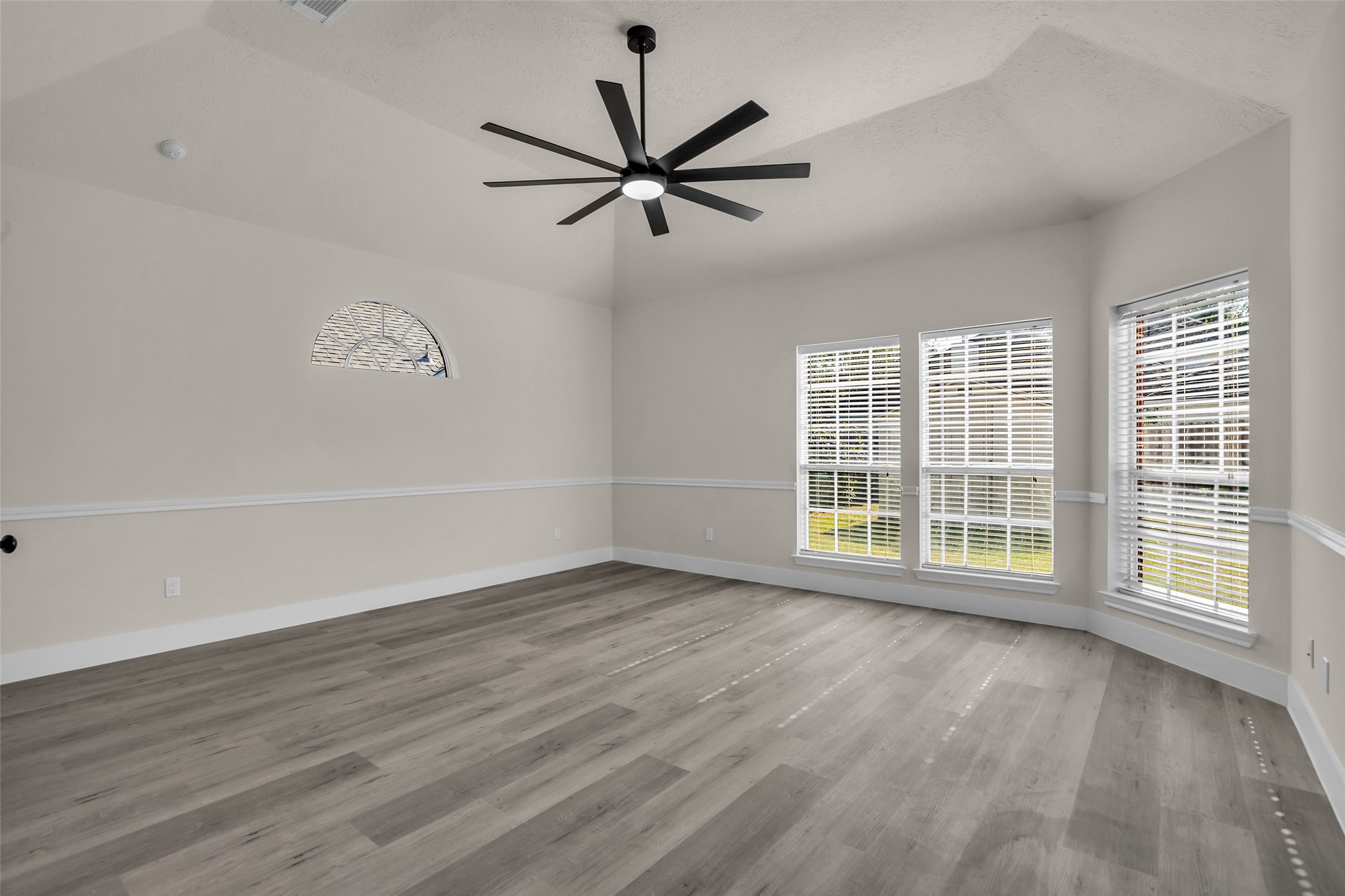 Spacious primary bedroom with elegant wood flooring, abundant natural light from large windows, and a modern ceiling fan adding a stylish touch.