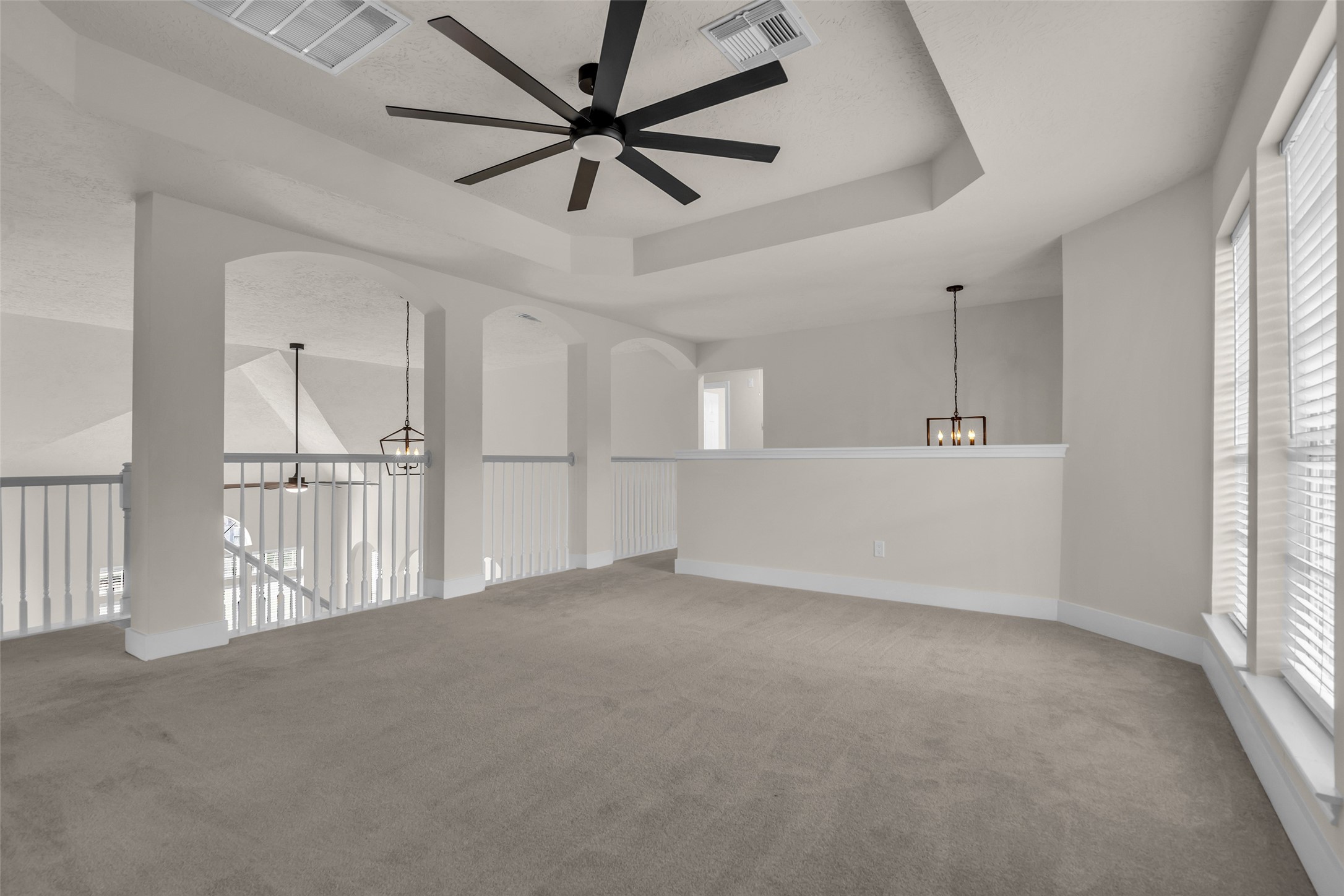 Open game room with abundant natural light, modern ceiling fan, and elegant railing overlooking the floor below, perfect for a versatile living area
