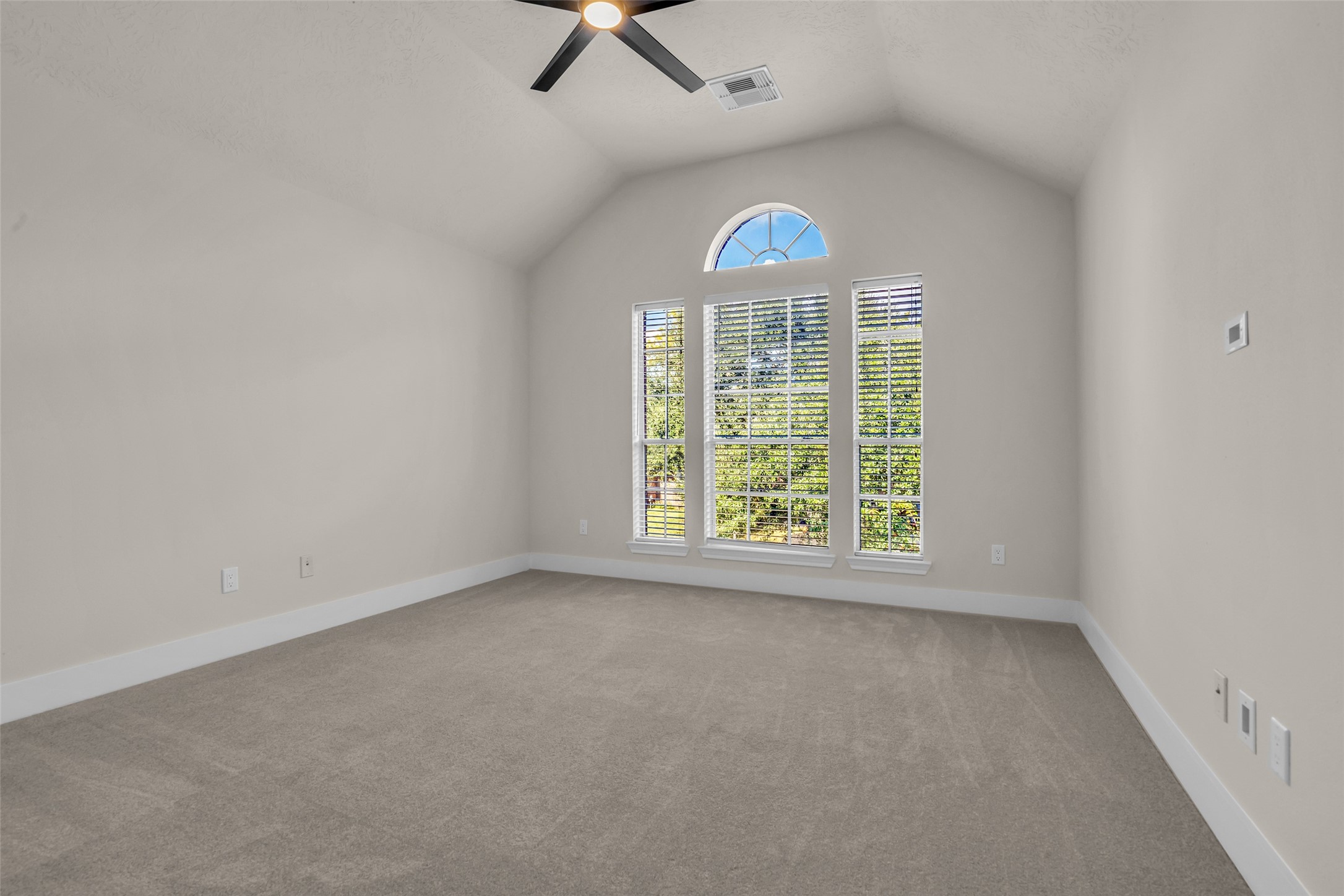 Third bedroom with vaulted ceilings, large arched window providing abundant natural light, and neutral carpeting, perfect for creating a cozy retreat.