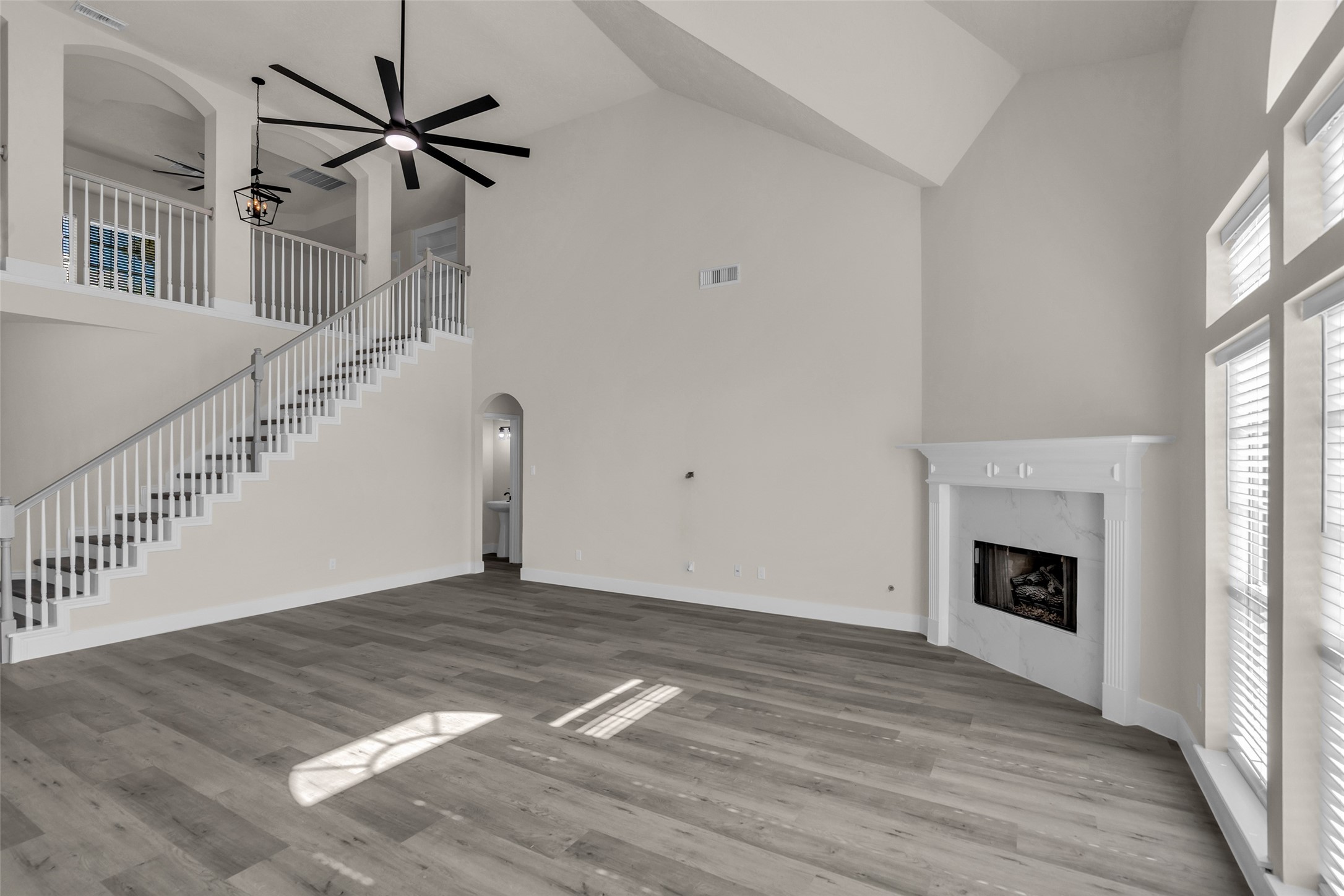 Spacious living room featuring high ceilings, elegant staircase, and a cozy fireplace, enhanced by abundant natural light from large windows.
