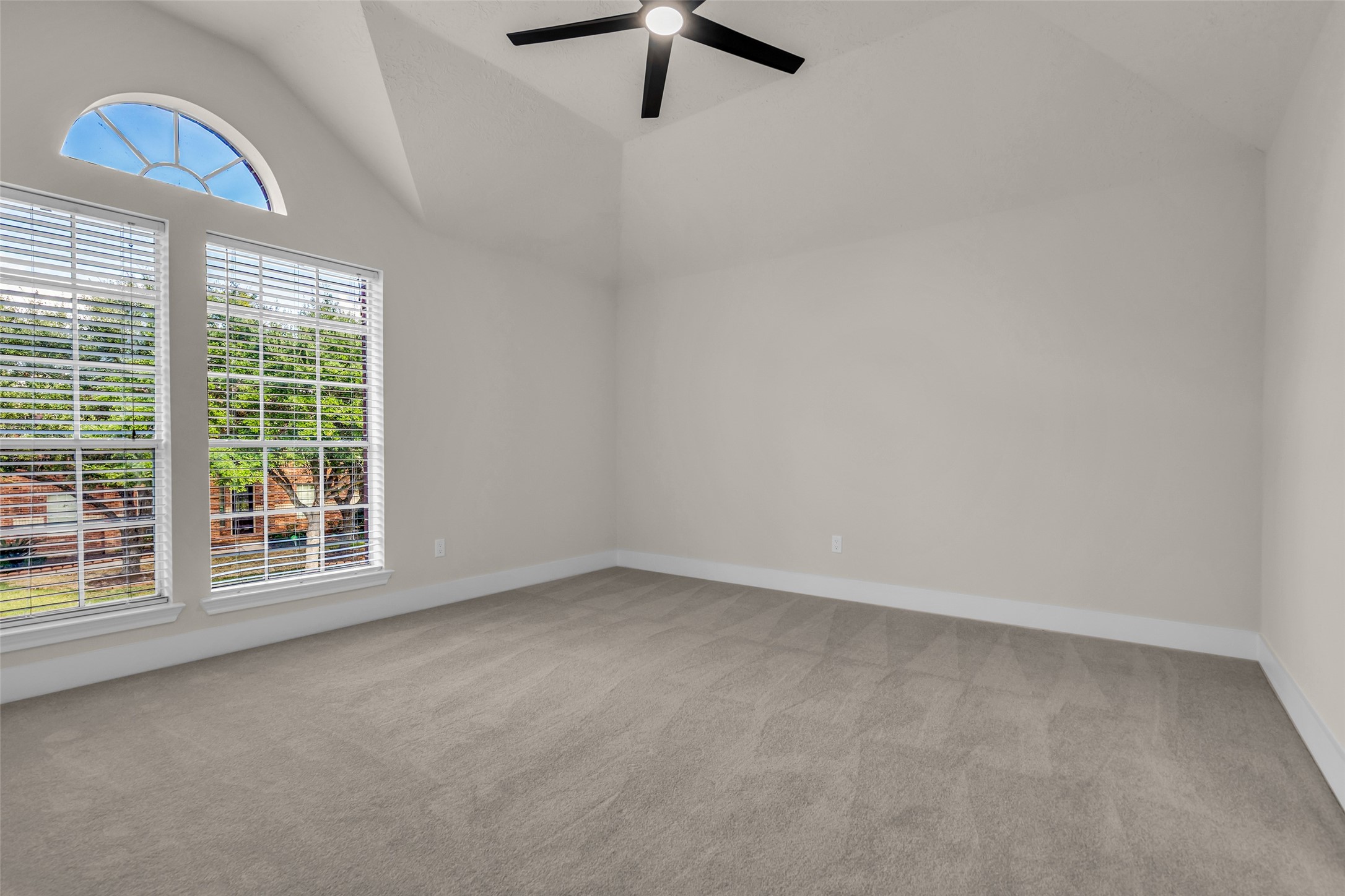 Spacious bedroom with vaulted ceilings, large arched window, and abundant natural light, complemented by neutral carpeting and a modern ceiling fan.