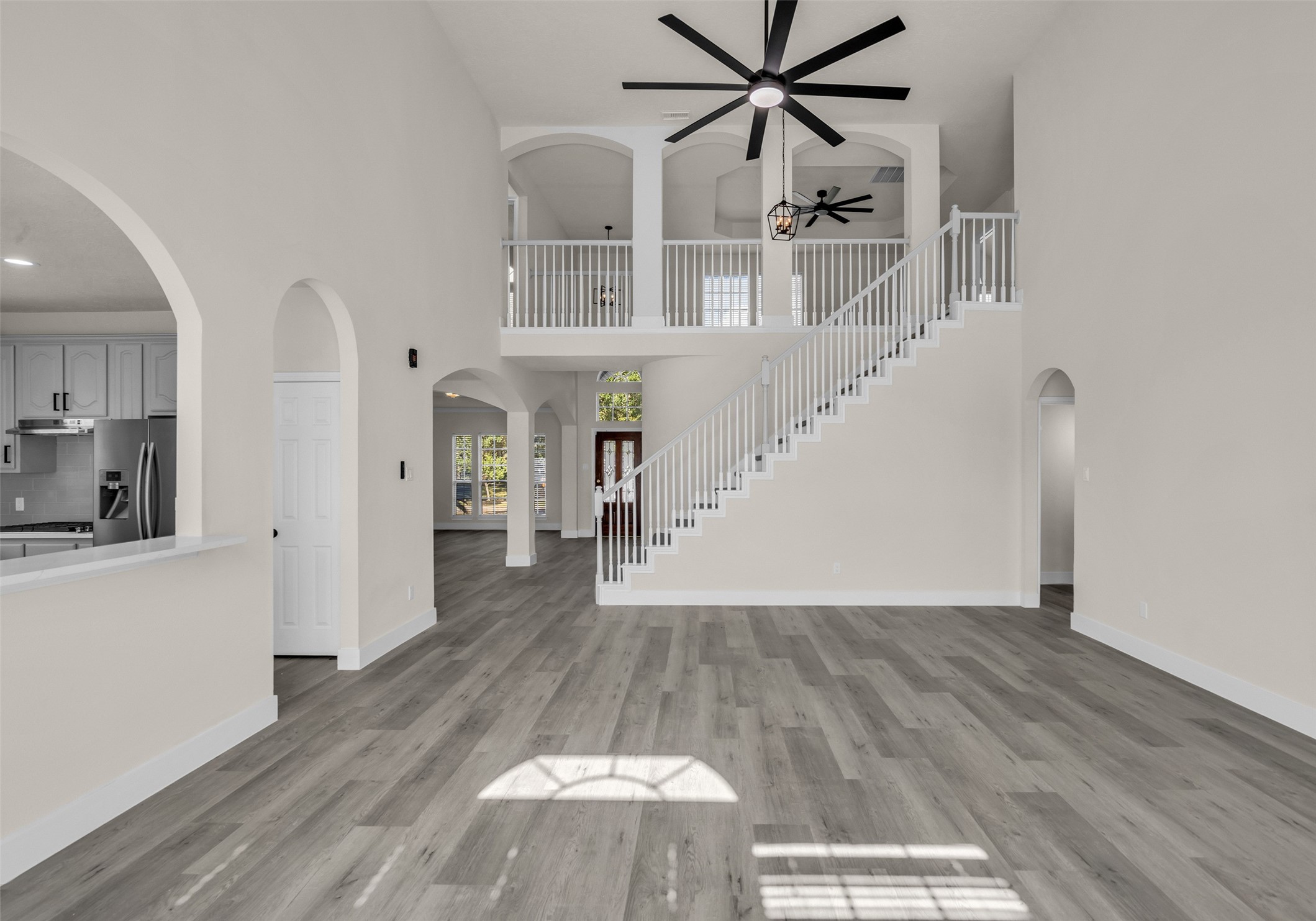 Stunning open living space with high ceilings, elegant staircase, and abundant natural light. The modern kitchen features sleek appliances and a breakfast bar, seamlessly connecting to the living area.
