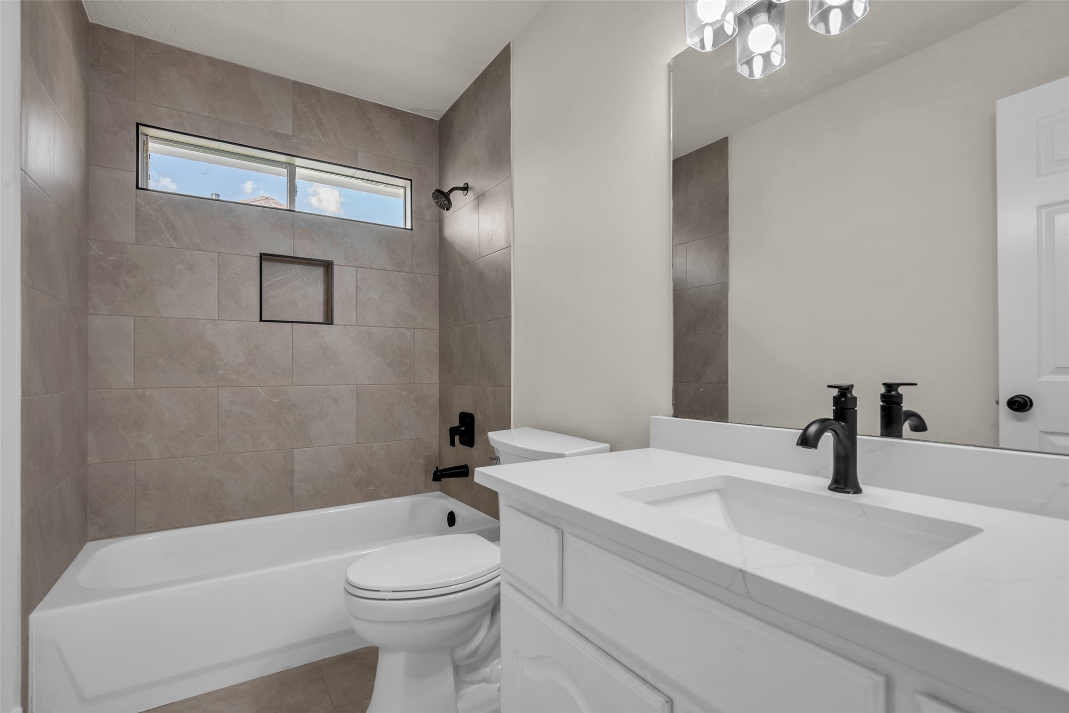 Another bathroom featuring sleek tiles, a spacious bathtub, and elegant black fixtures, complemented by a bright, clean vanity area.