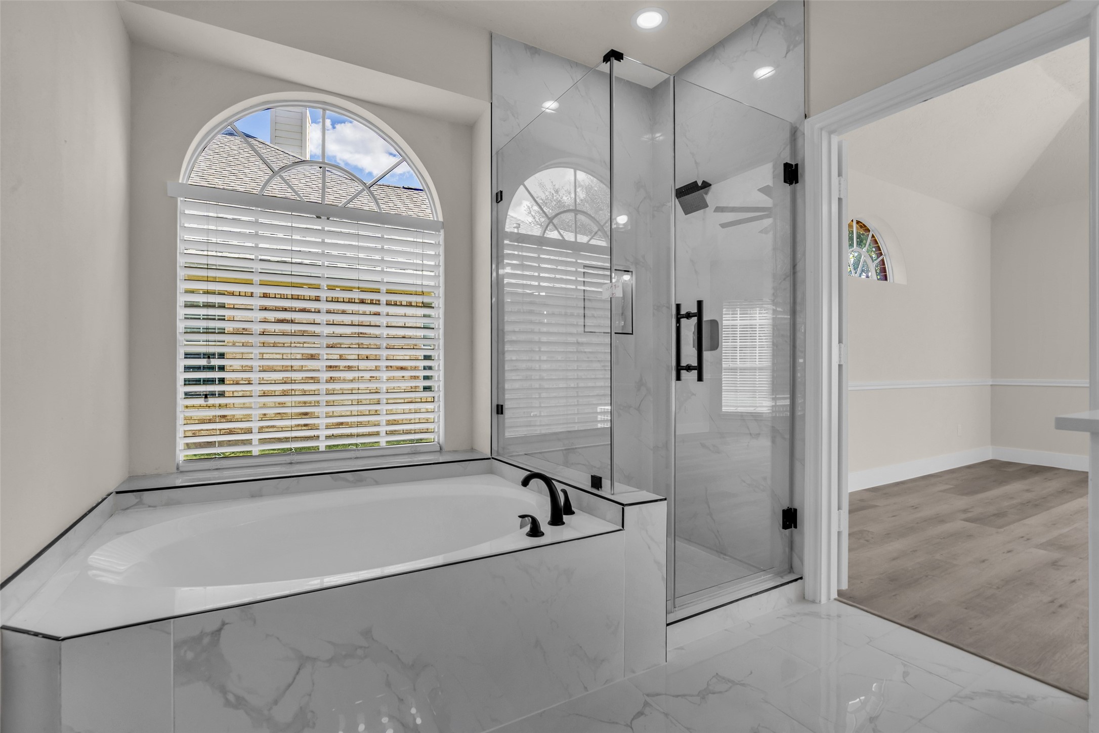 Luxurious bathroom featuring a sleek glass-enclosed shower and a spacious soaking tub, complemented by elegant marble tile and arched windows for natural light.