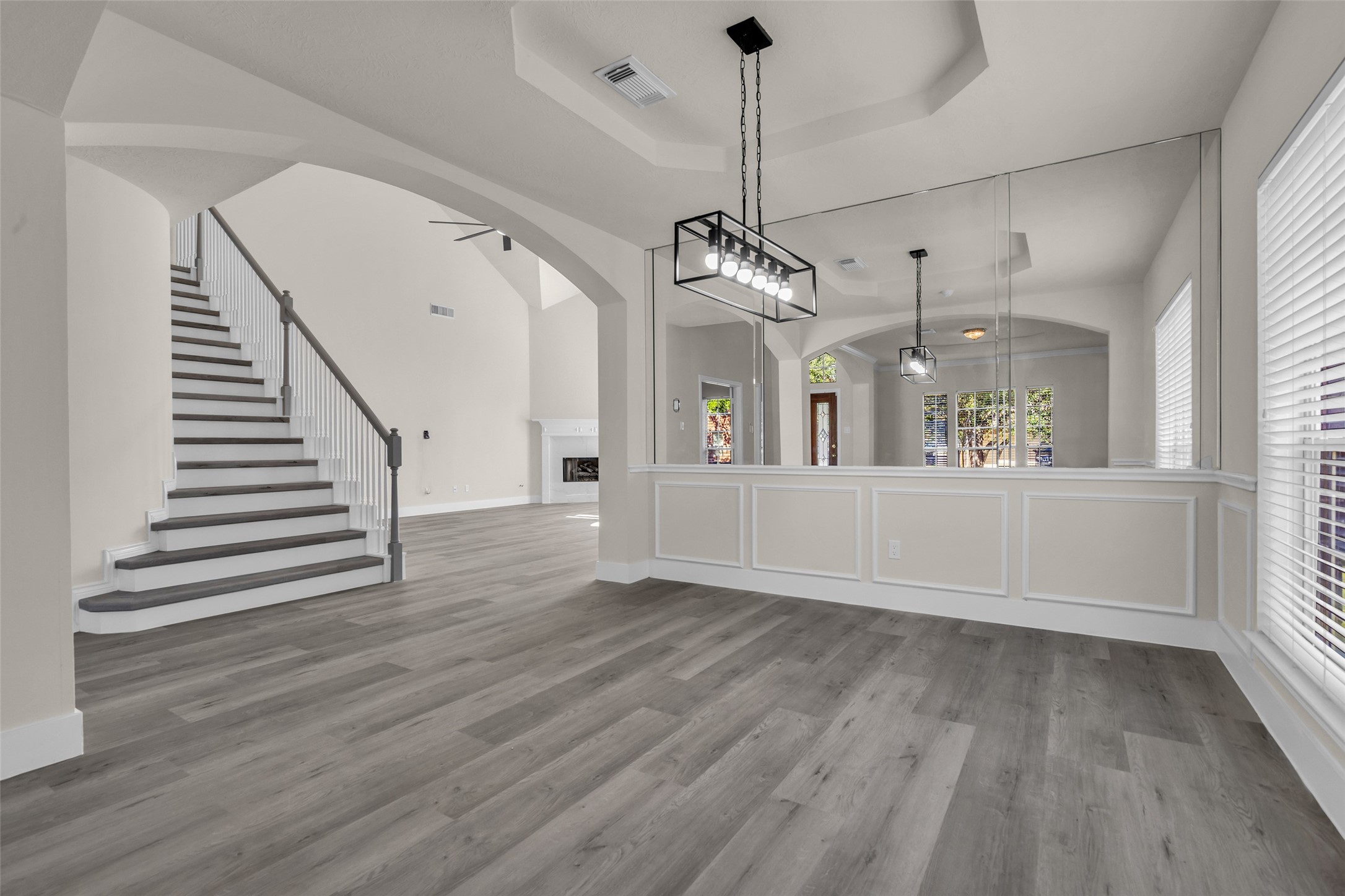 Elegant open-concept living area with high ceilings, modern lighting, and a graceful staircase. The space features large windows and sleek wood flooring, creating a bright and inviting atmosphere.
