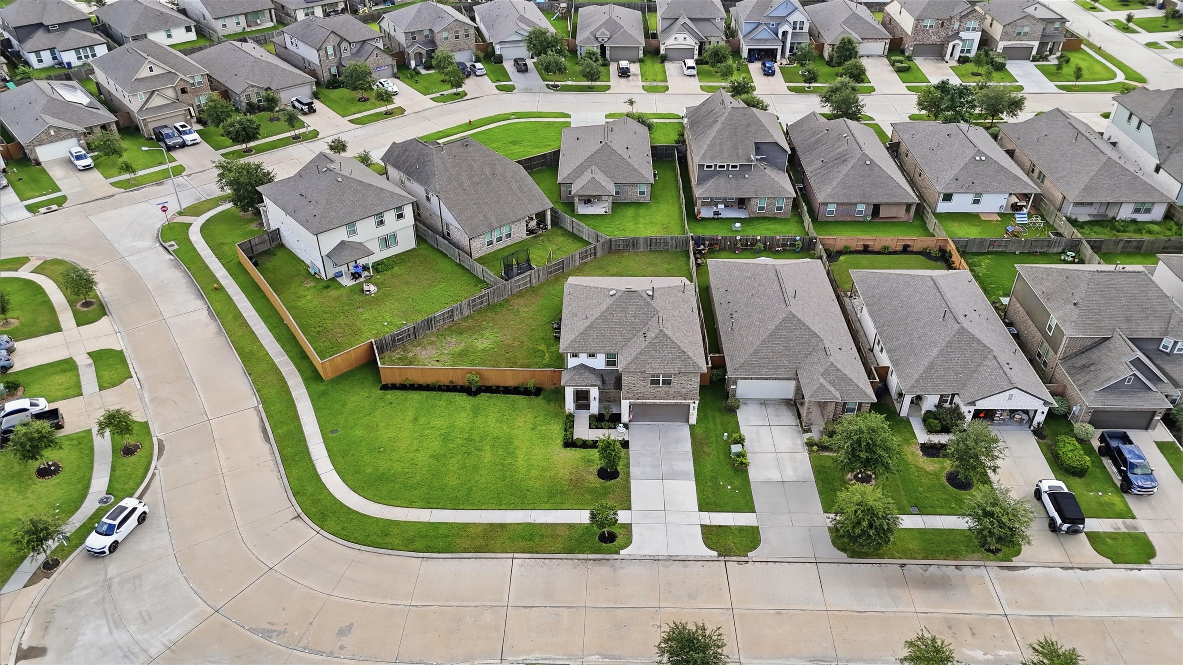 Aerial photo showcases a suburban neighborhood with well-maintained homes. The area has neatly landscaped lawns and is situated on a winding street, offering a peaceful and organized residential setting.