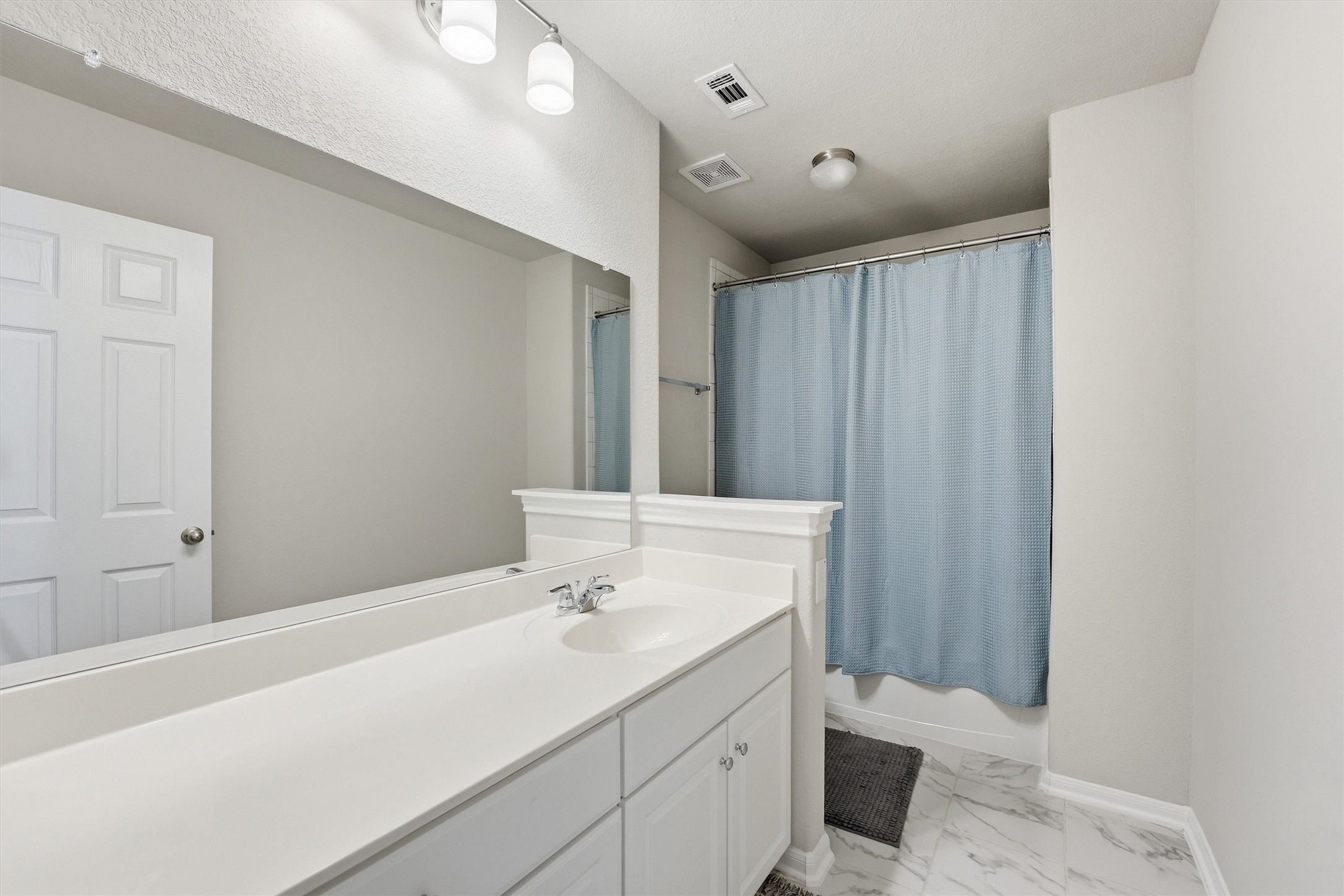 Secondary bathroom features a clean, modern design with a large mirror, white vanity, shower and tub combo.