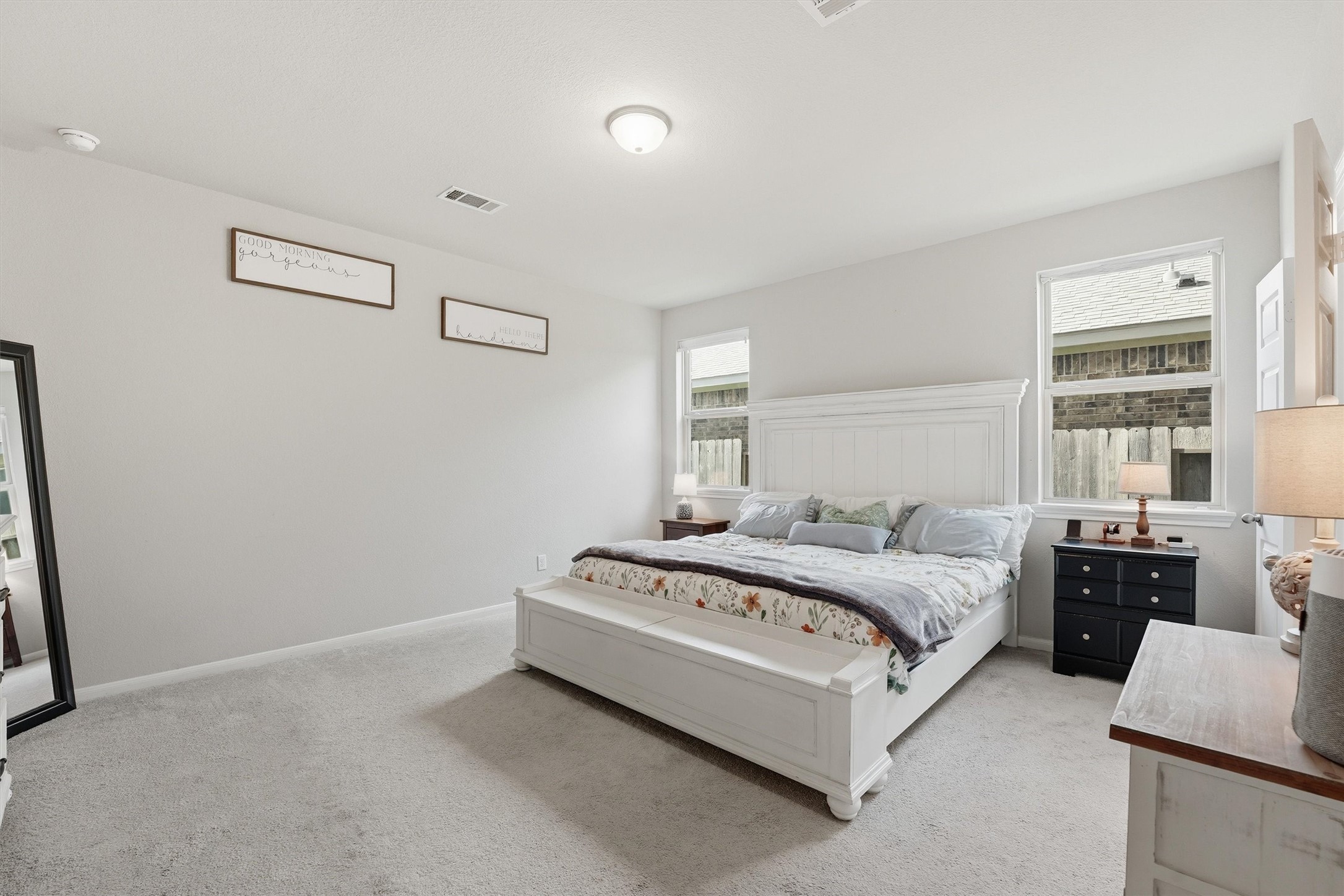 Spacious primary bedroom with neutral tones, ample natural light from two windows, and a cozy carpet.