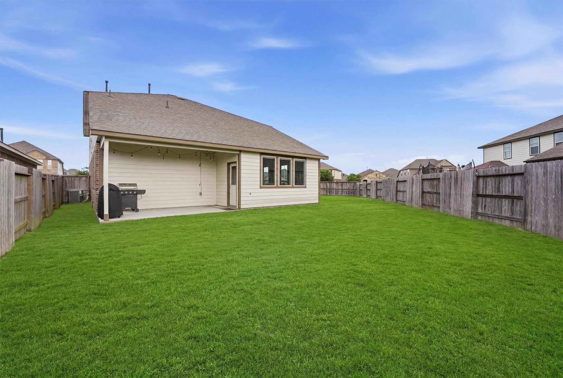 Spacious backyard with well-maintained lawn, a covered patio area, and wooden fencing, perfect for outdoor activities and entertaining.