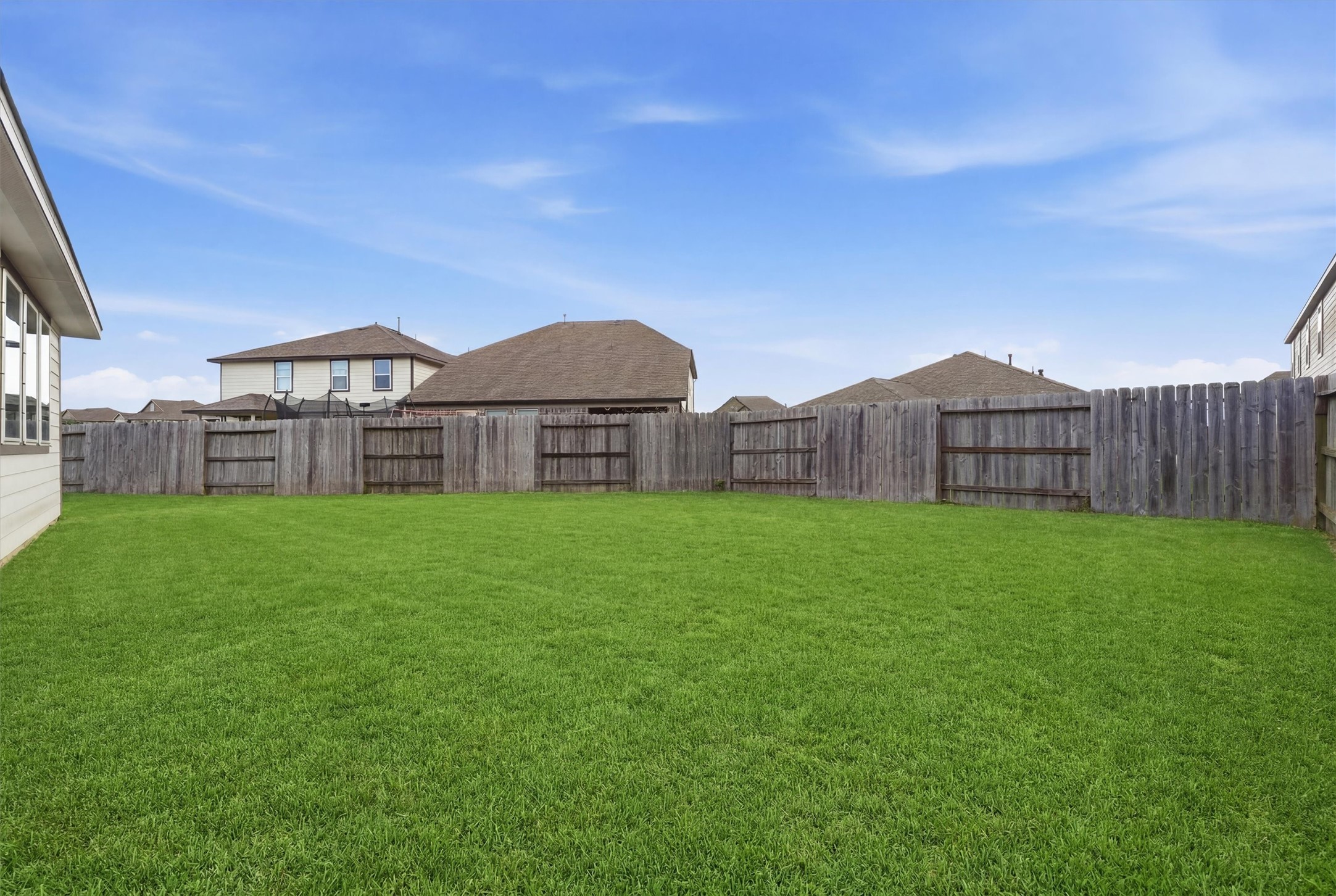 Pool sized backyard with a well-maintained lawn, enclosed by a wooden privacy fence, ideal for outdoor activities and gardening.