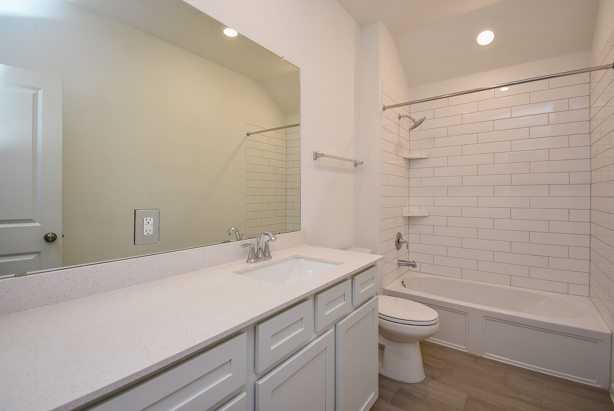 The upstairs, shared, hall bathroom featuring a large vanity with quartz countertops, white cabinetry, and a wide mirror. The shower/tub combo is accented with sleek subway tile and built-in shelving, while recessed lighting enhances the bright and clean design.