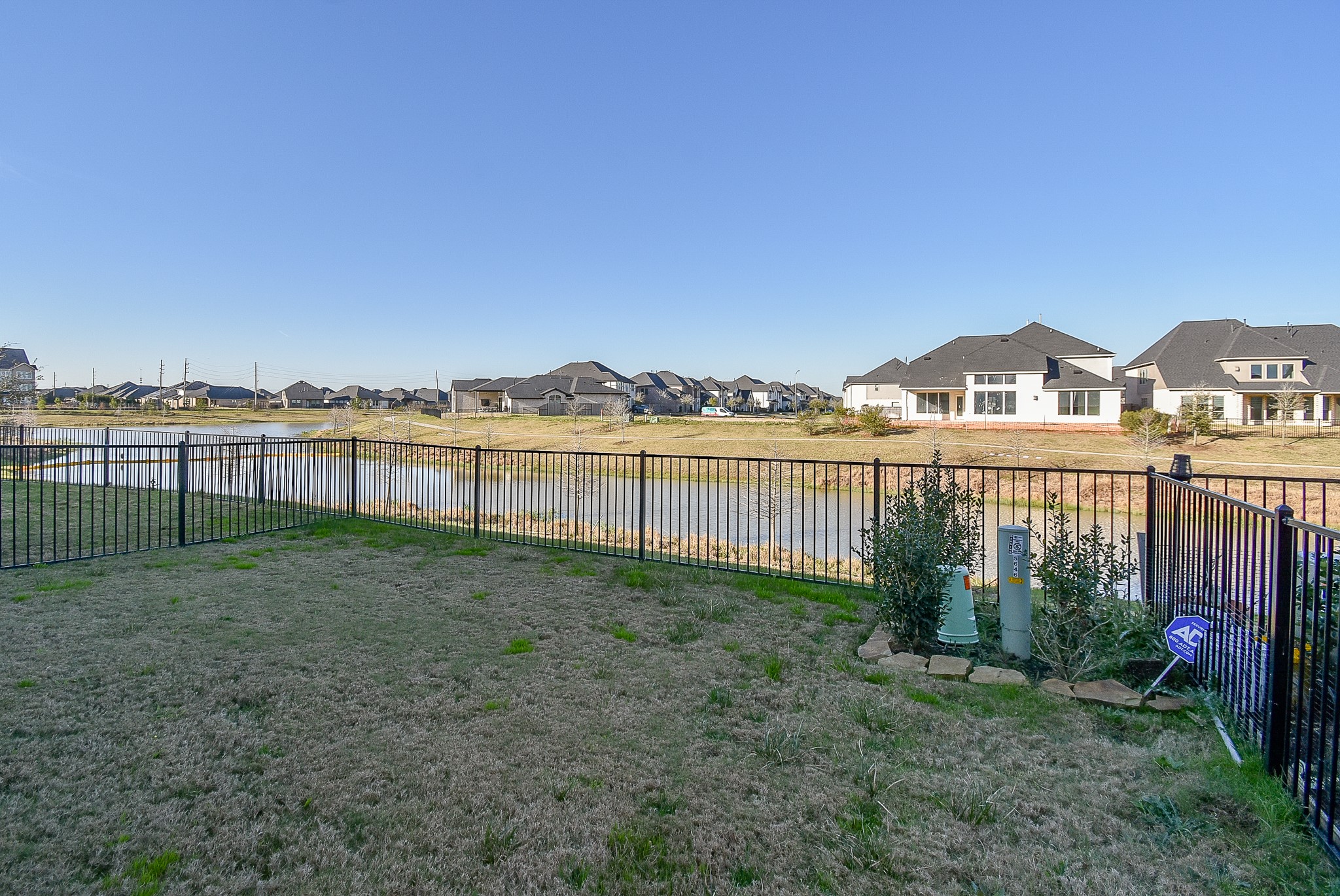 A scenic backyard with a wrought iron fence, offering beautiful water views of a community lake. The open space provides a serene setting, with small landscaped area in the corner.