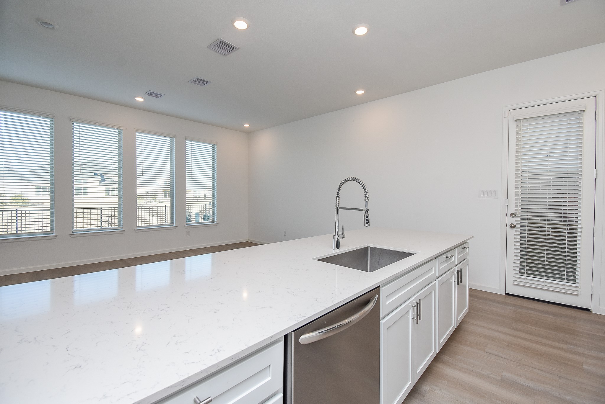 A large quartz island with a stainless steel dishwasher, deep sink, and high-arc pull-down faucet. The white drawers cabinets feature stylish hardware and are soft close. The door leads to the side and back yard.
