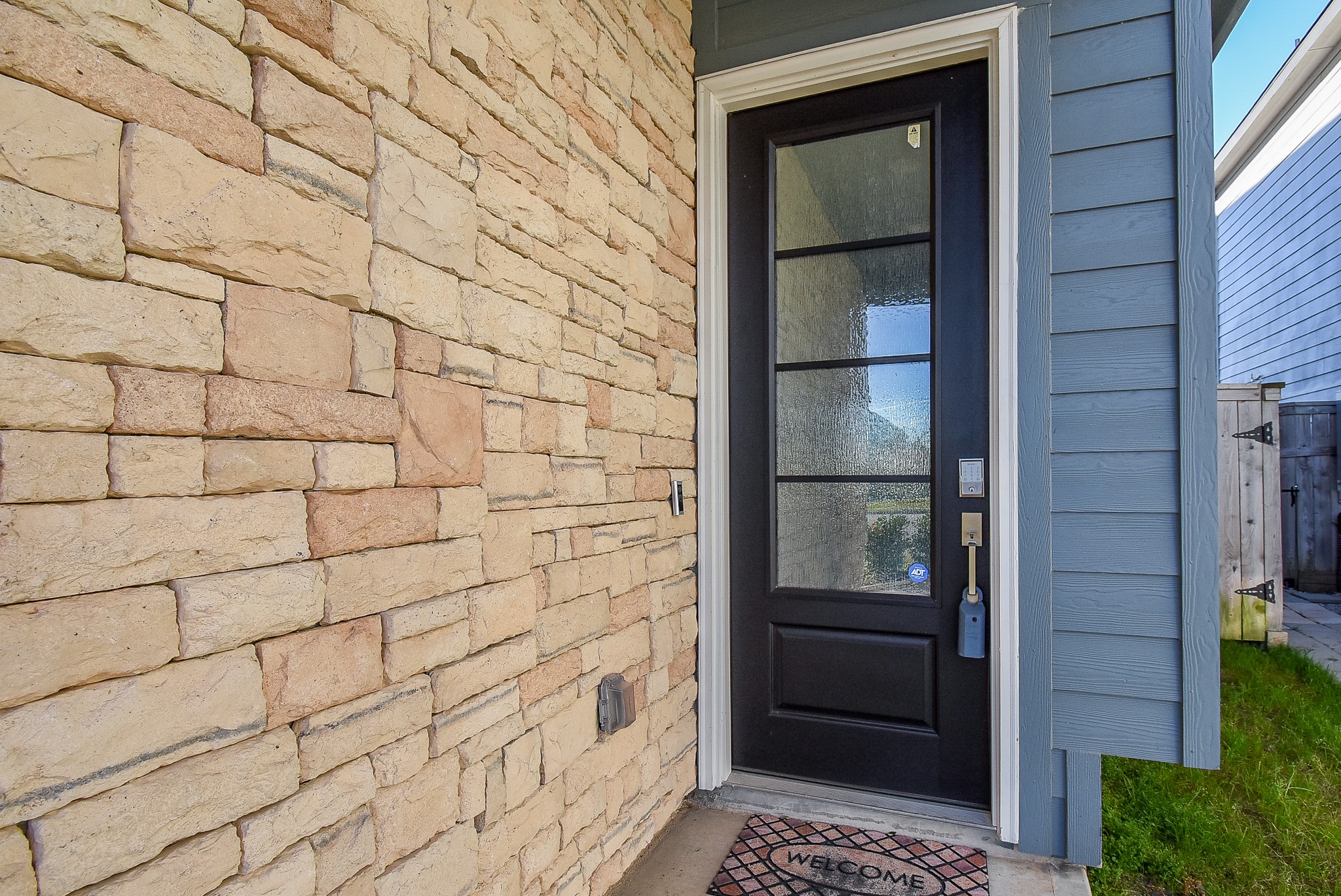 A modern front entrance with a black door featuring textured glass panels, complimented by stone veneer, with a smart keypad lock