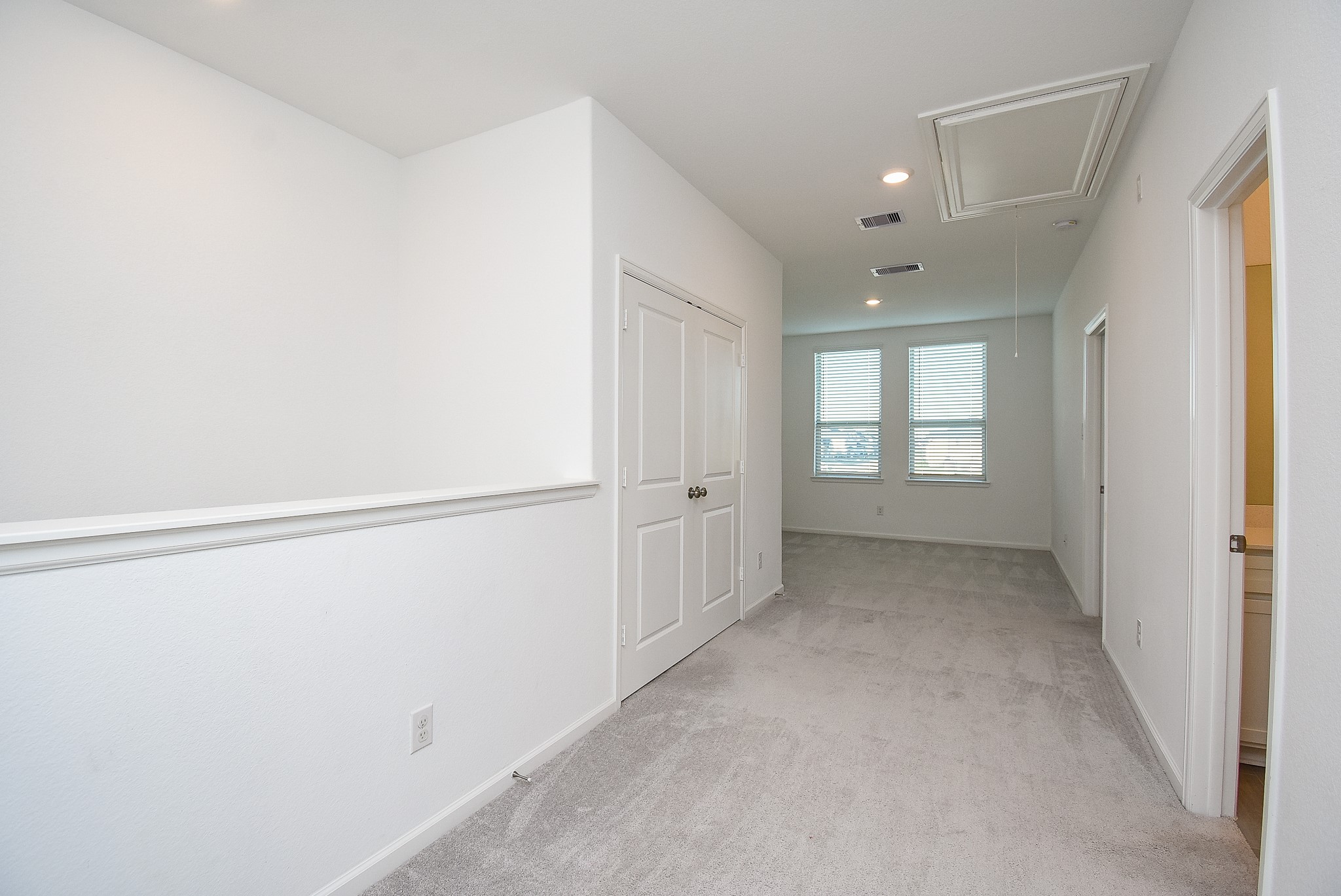 A bright upstairs hallway with neutral carpeting and white walls, leading to additional rooms and the flex space.
