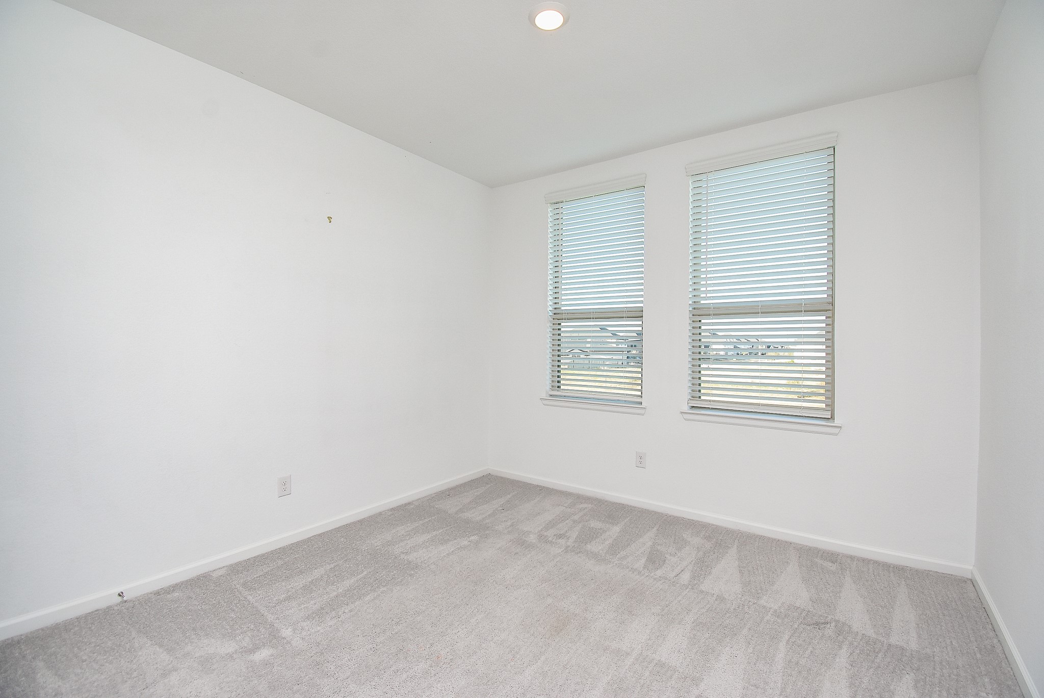 A bright and versatile upstairs flex space featuring neutral carpeting, recessed lighting, and two large windows with blinds, allowing for plenty of natural light. Ideal for use as a home office, family room or play area with a modern, open feel.