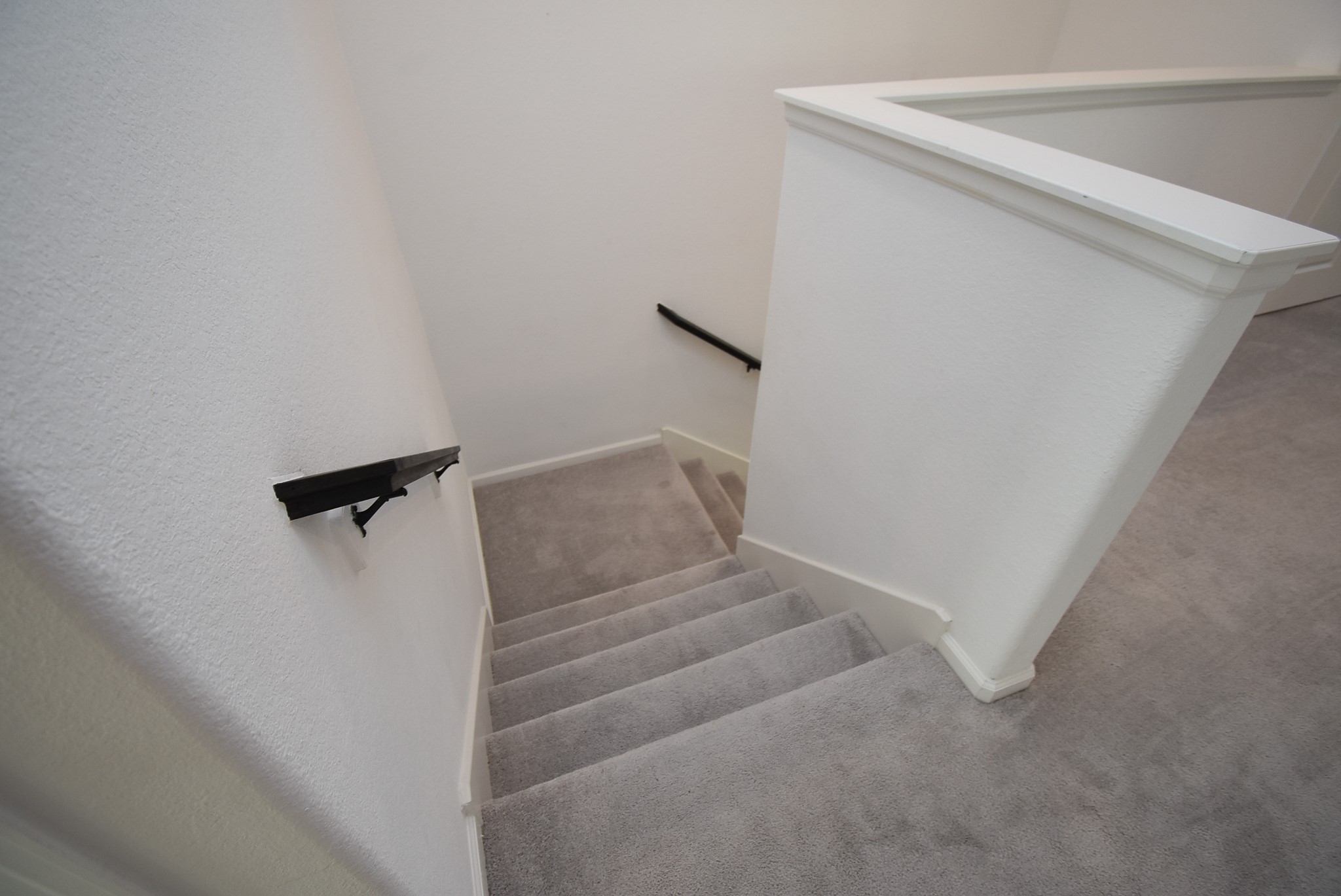 A carpeted staircase with black handrails, lead you to the upper level.