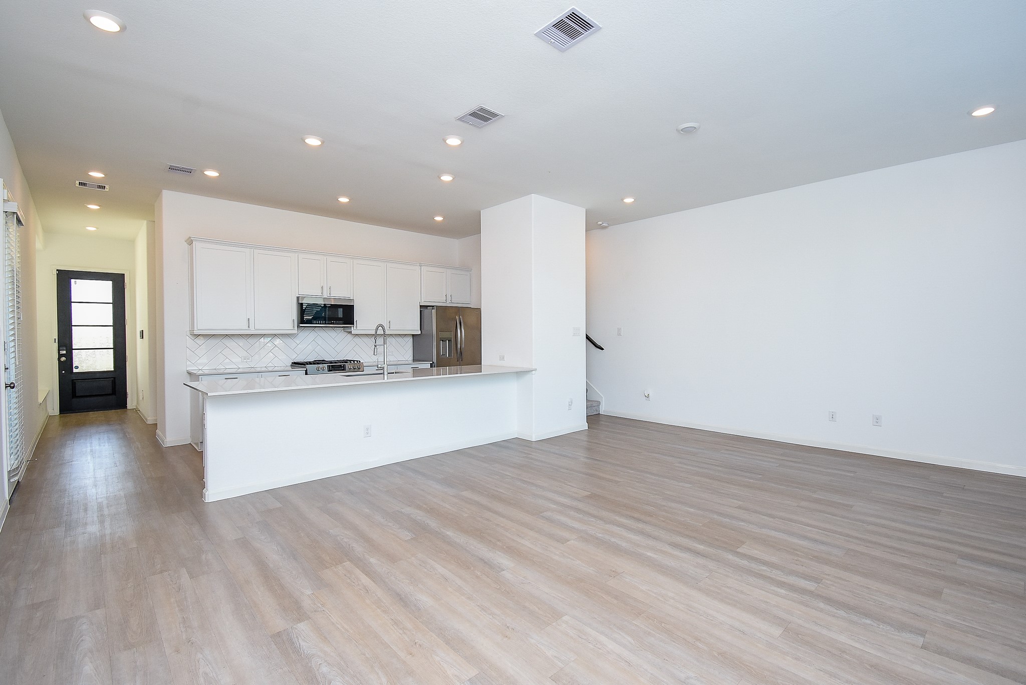 The kitchen island with a bar for stools, seamlessly flows into the dining space and family room, creating an inviting and functional living space with modern finishes and recessed lighting.