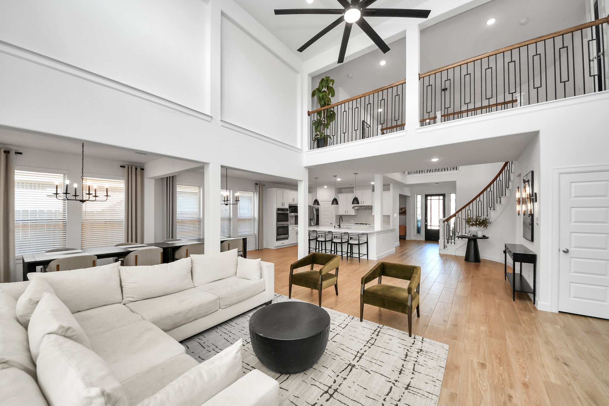 Spacious open-concept living area with high ceilings, modern finishes, and ample natural light, featuring a stylish kitchen, elegant staircase, and cozy seating perfect for entertaining. Spacious open-concept living area with high ceilings, modern finishes, and ample natural light, featuring a stylish kitchen, elegant staircase, and cozy seating perfect for entertaining.