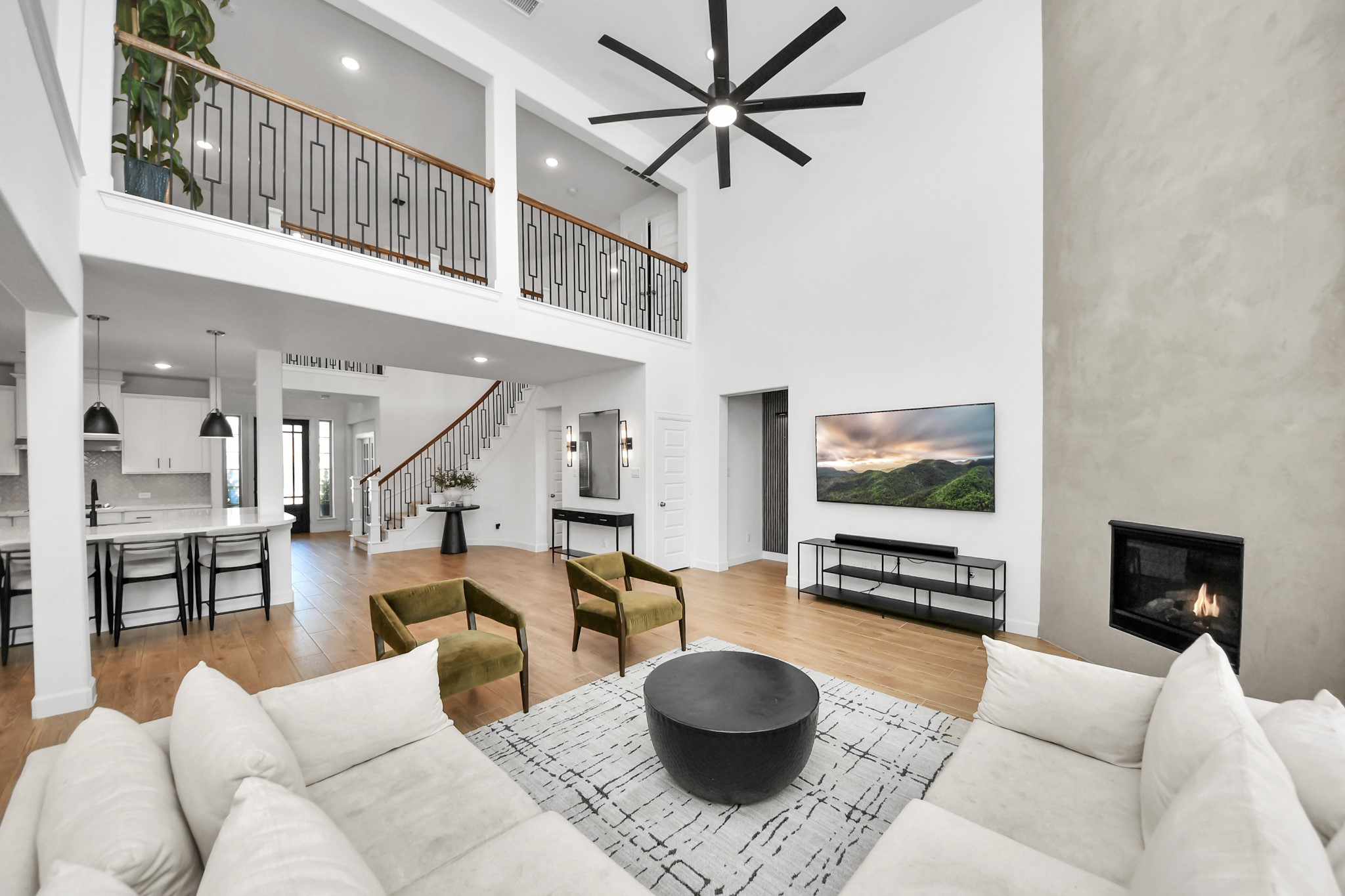 Stunning open-concept living room featuring soaring ceilings, a modern fireplace, and abundant natural light, seamlessly flowing into a sleek kitchen with a large island and contemporary finishes. Stunning open-concept living room featuring soaring ceilings, a modern fireplace, and abundant natural light, seamlessly flowing into a sleek kitchen with a large island and contemporary finishes.