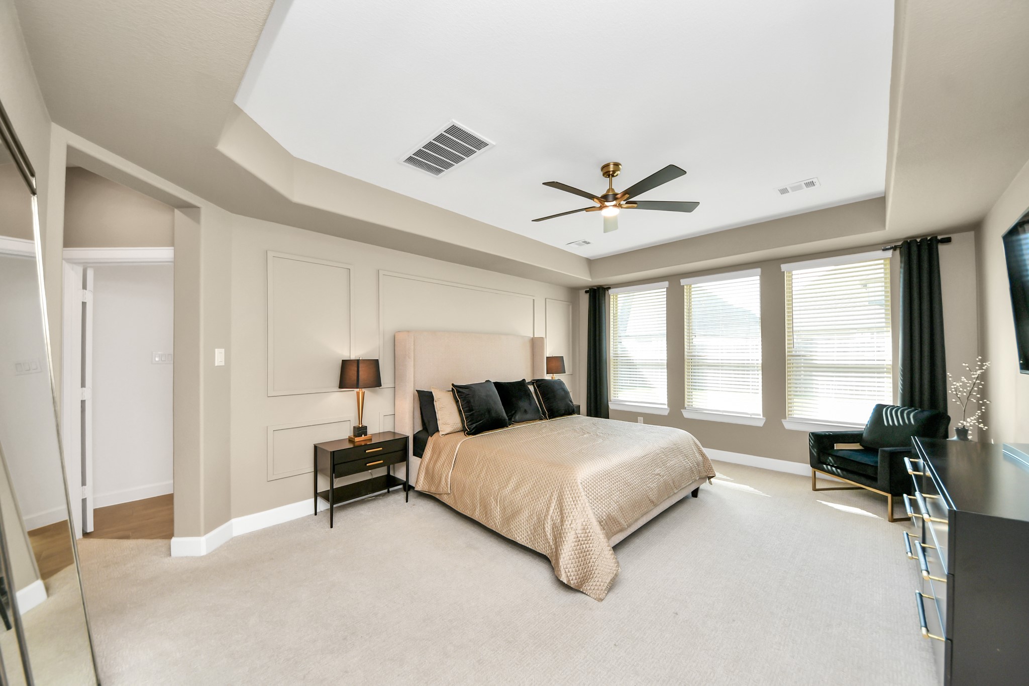 Spacious bedroom with a tray ceiling, ample natural light from multiple windows, and elegant neutral decor.