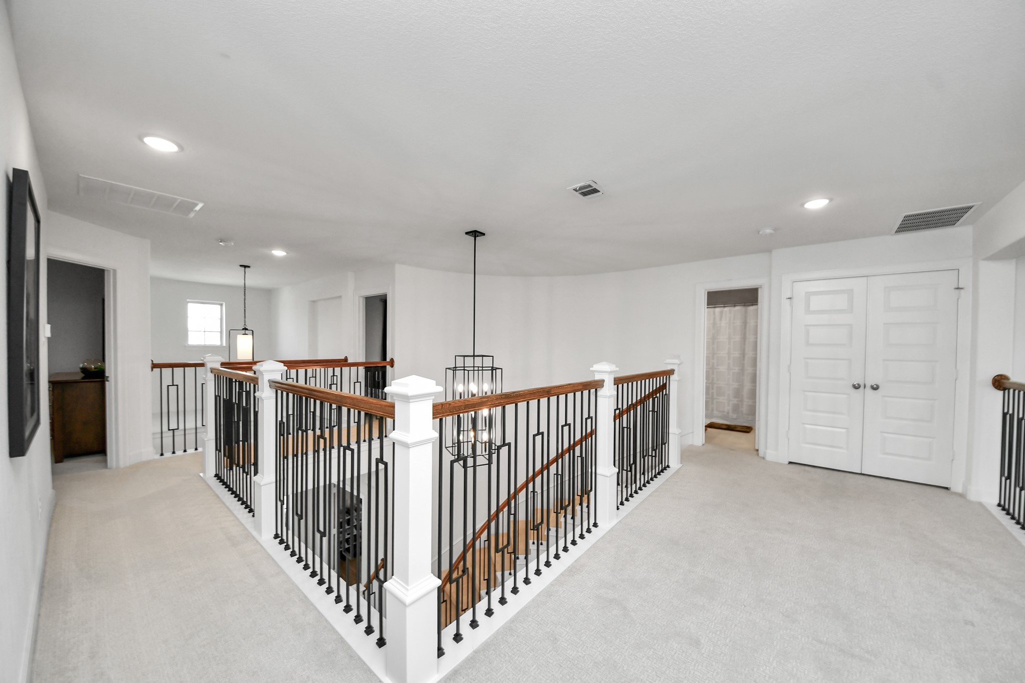 Spacious upstairs hallway with elegant iron railing, modern light fixtures, and plush carpeting.