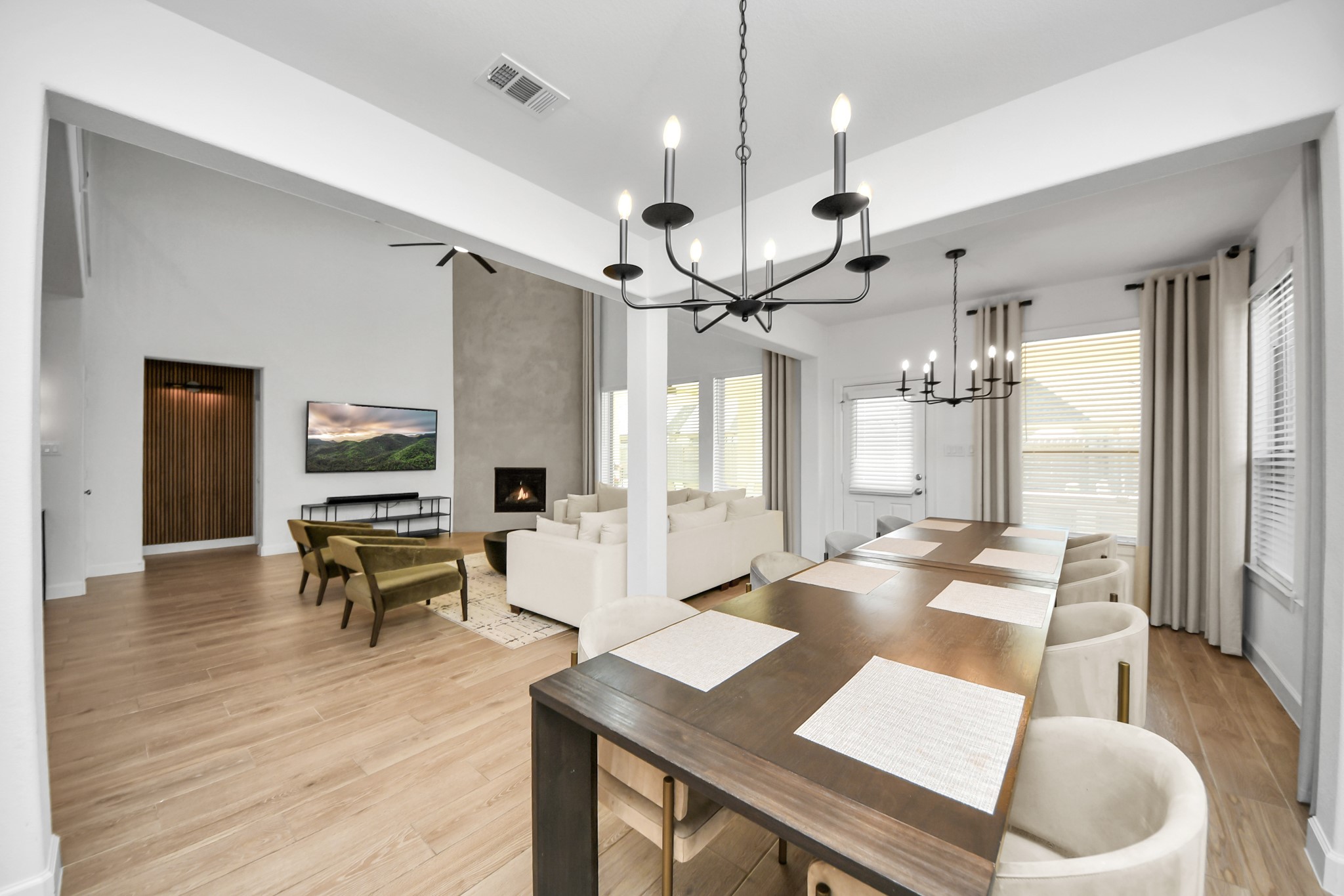 Spacious open-concept living and dining area with elegant chandeliers, a cozy fireplace, and natural light streaming through large windows.