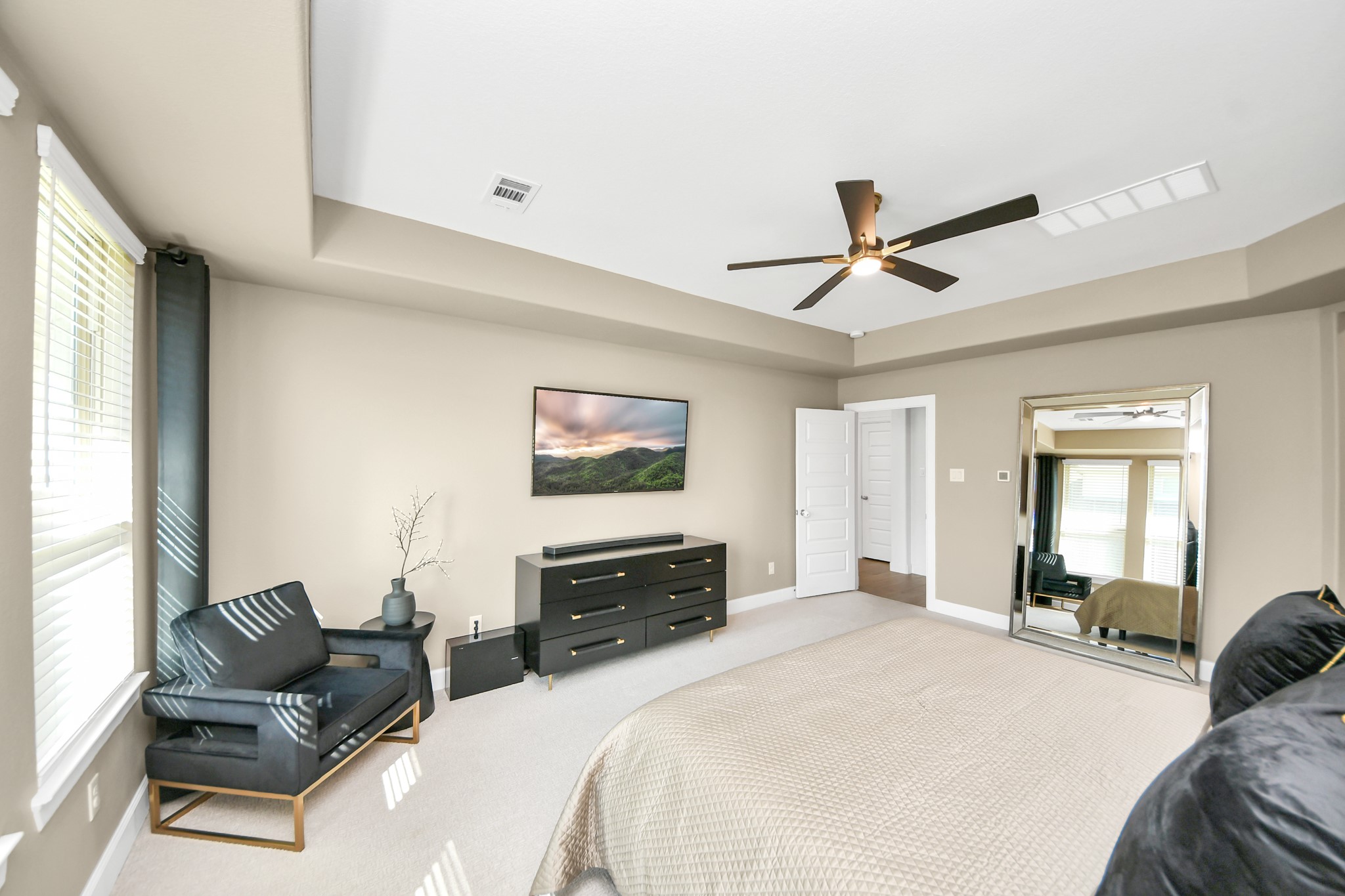 Spacious primary bedroom with abundant natural light, featuring a cozy sitting area, modern ceiling fan, and large mirror to enhance the open feel.