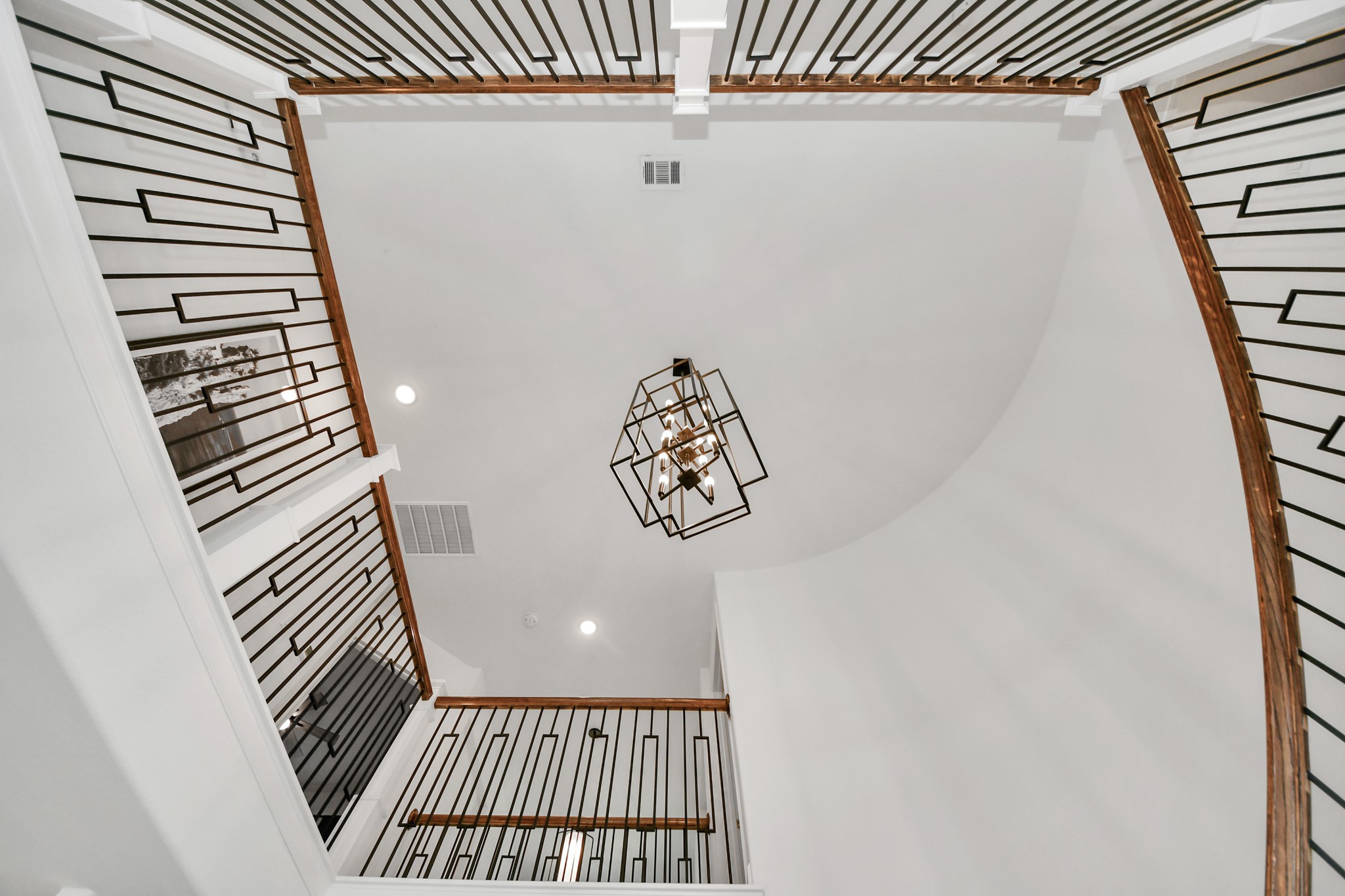 Stunning two-story foyer with elegant geometric railing and a modern chandelier, creating a grand and stylish entrance.
