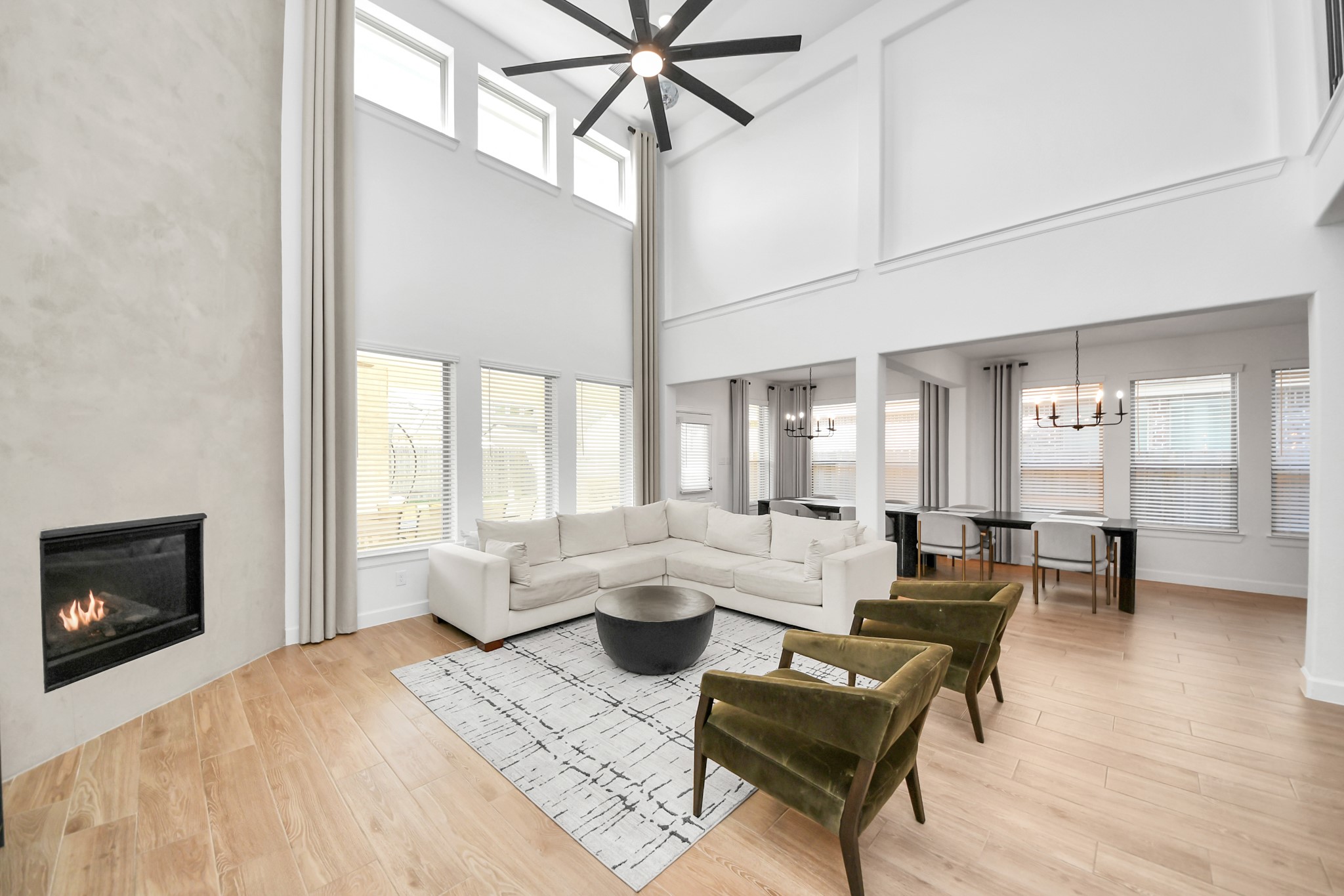 Stunning two-story living area features a cozy fireplace, expansive windows for abundant natural light, custom two-story curtains, and elegant hardwood floors, seamlessly connecting to a stylish dining space. Stunning two-story living area features a cozy fireplace, expansive windows for abundant natural light, custom two-story curtains, and elegant hardwood floors, seamlessly connecting to a stylish dining space.