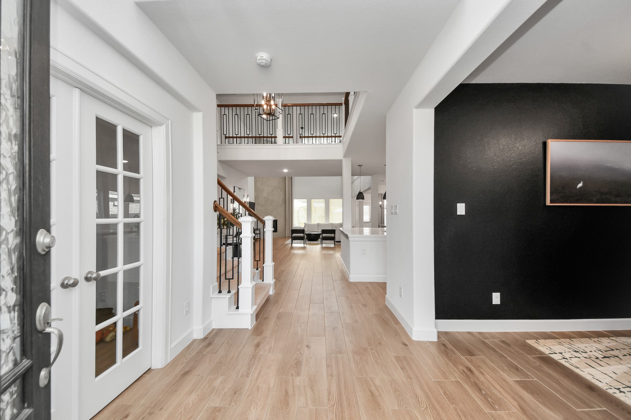Elegant front entrance view with sleek wood flooring, French doors, and a view into the spacious, open-plan living area featuring a modern staircase and stylish black accent wall.