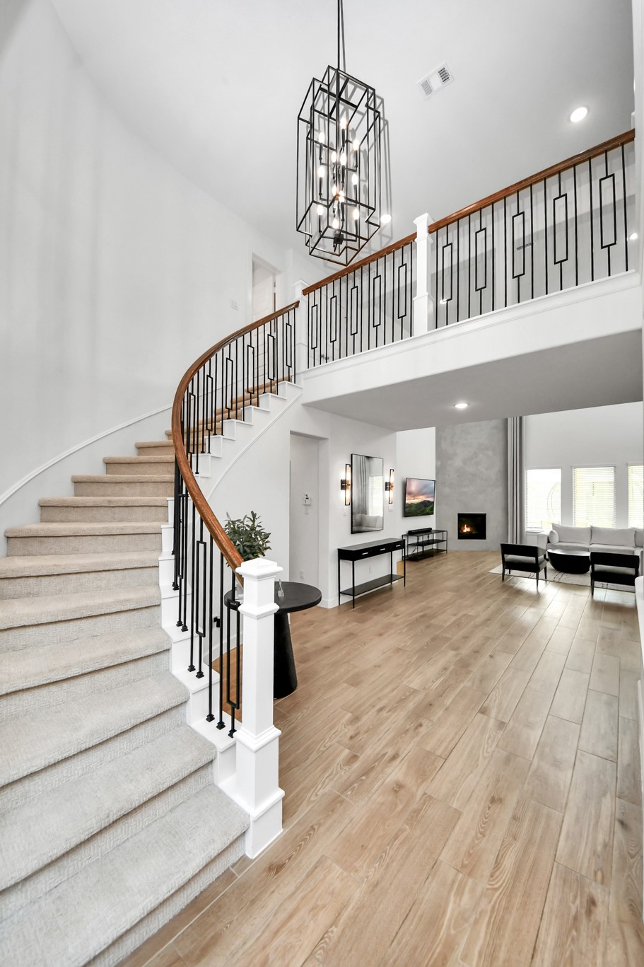 Elegant foyer featuring a sweeping staircase with a modern wrought-iron railing, complemented by a striking chandelier and warm wood flooring.