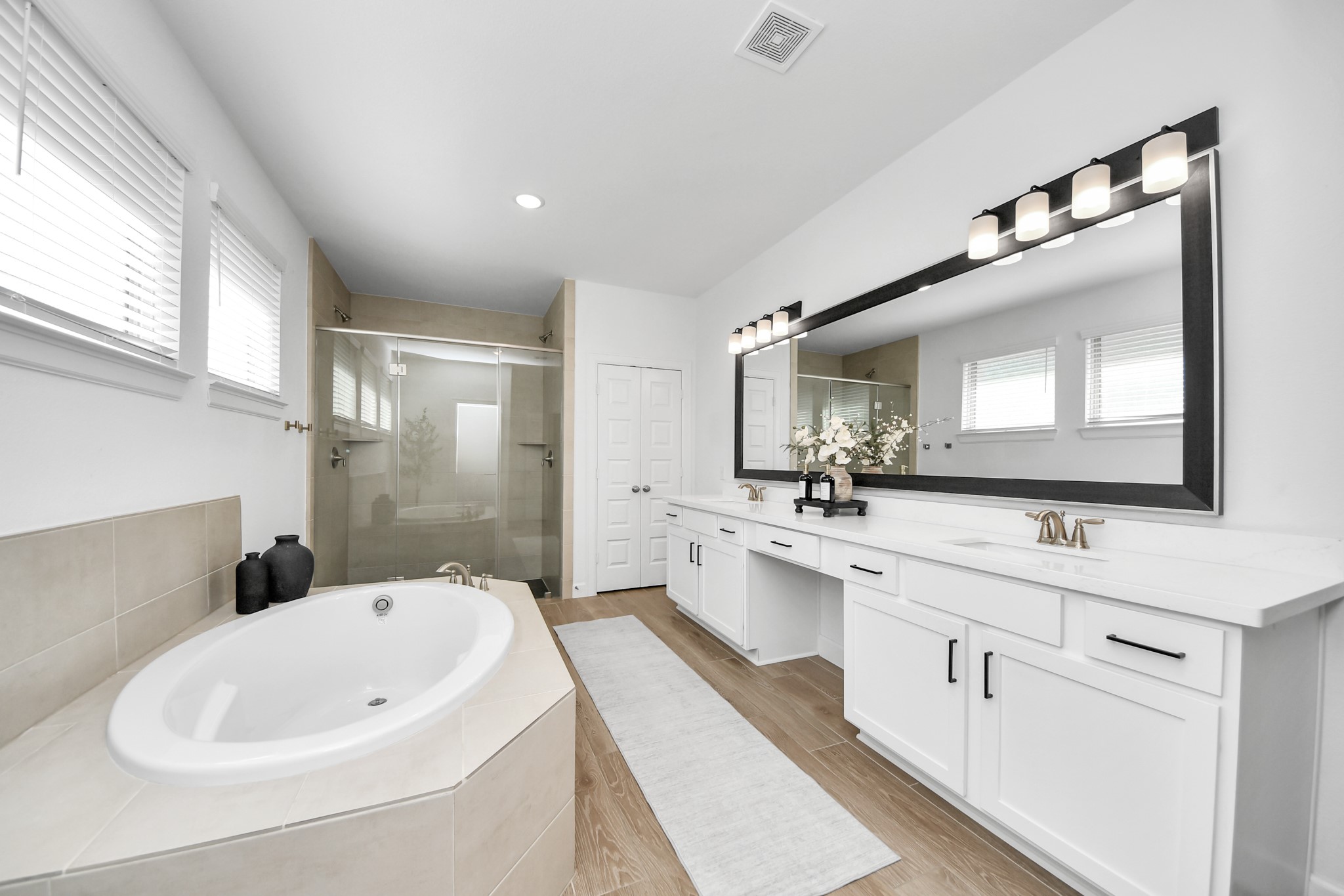 Elegant bathroom featuring a spacious double vanity with modern fixtures, a luxurious soaking tub, and a sleek glass-enclosed shower, all enhanced by abundant natural light.