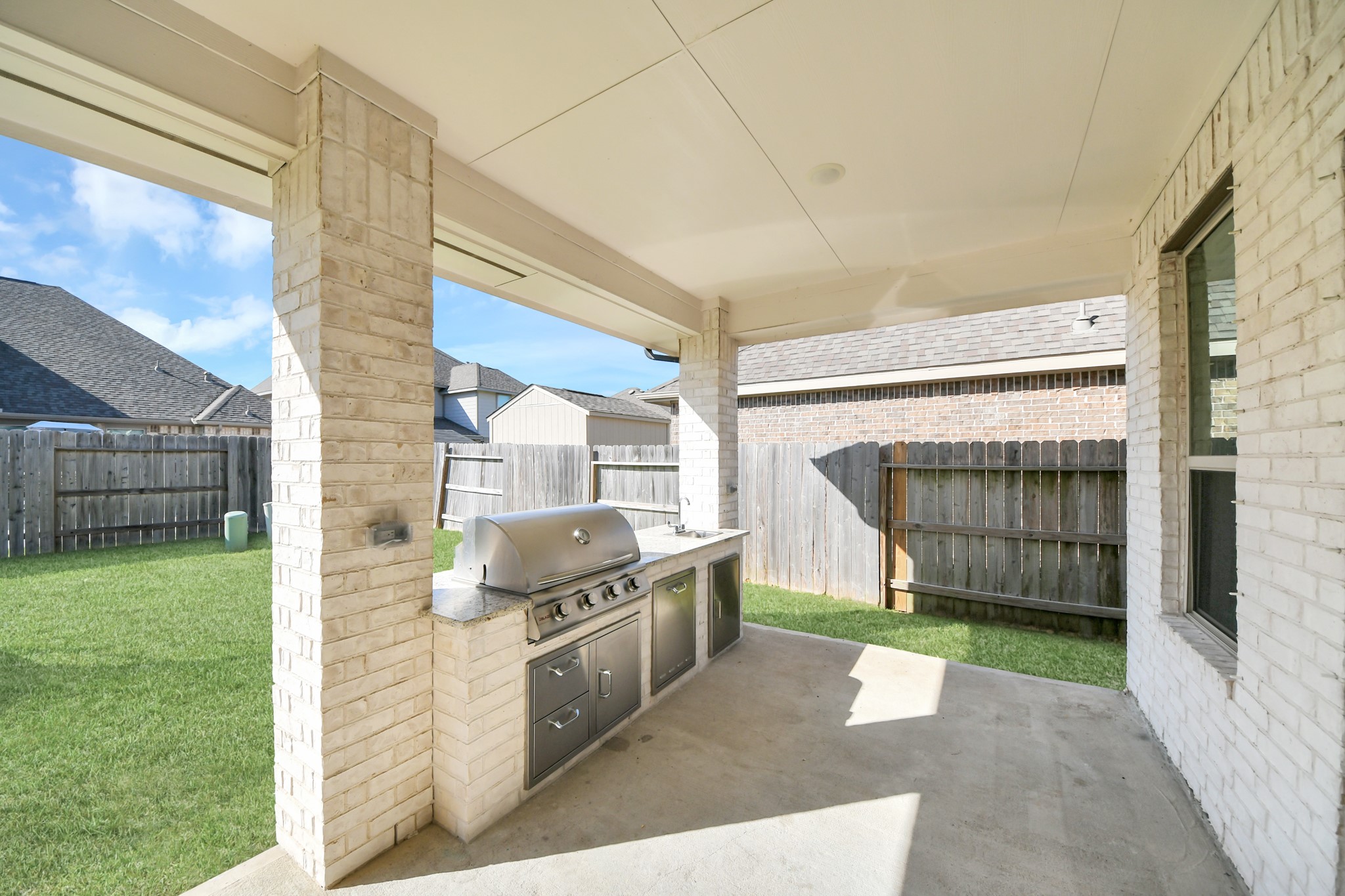 Spacious covered patio featuring a built-in outdoor grill and ample room for entertaining in a private fenced yard.