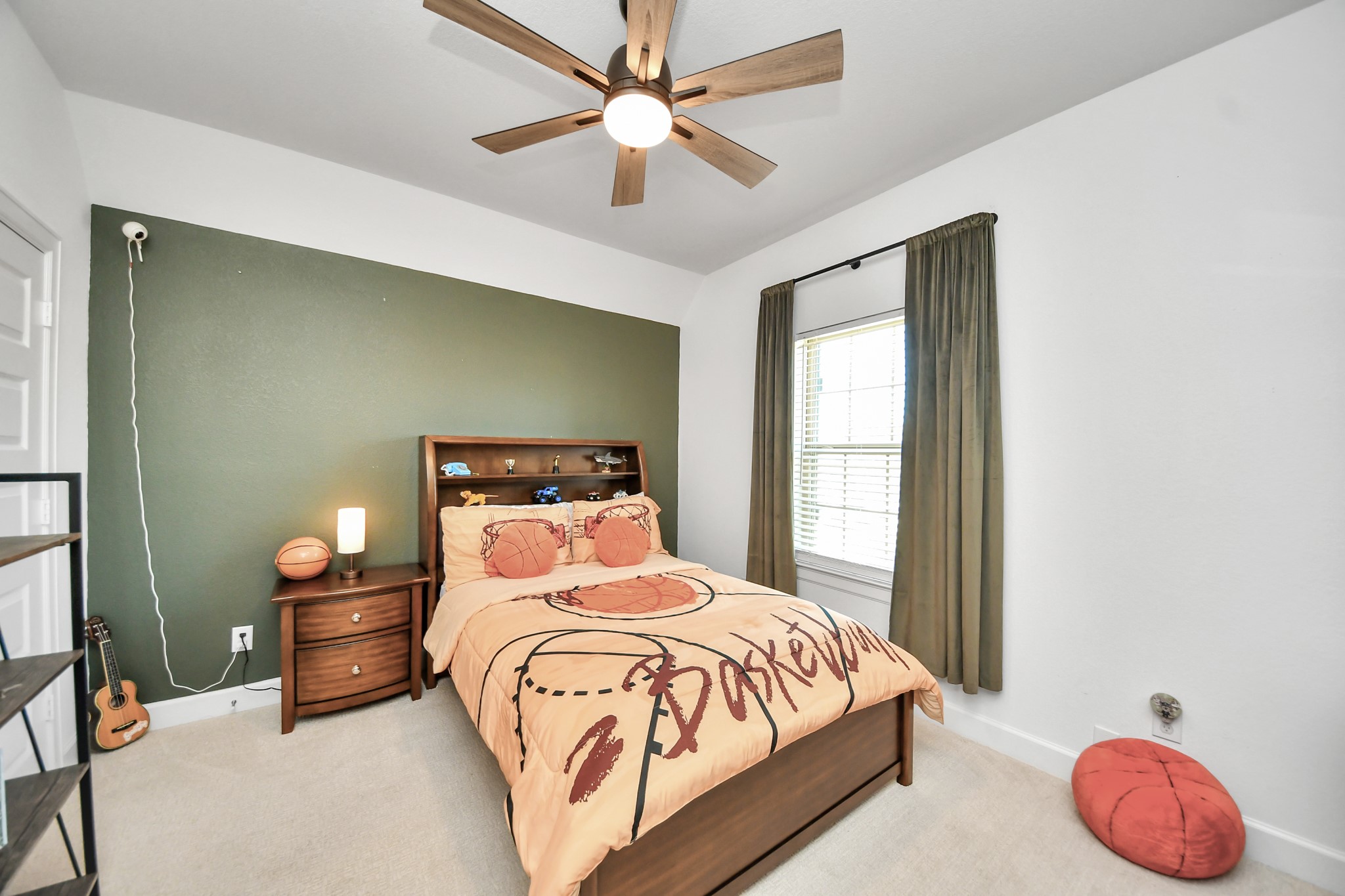Cozy bedroom featuring a basketball-themed decor, accentuated by a warm green accent wall and ample natural light from a large window.