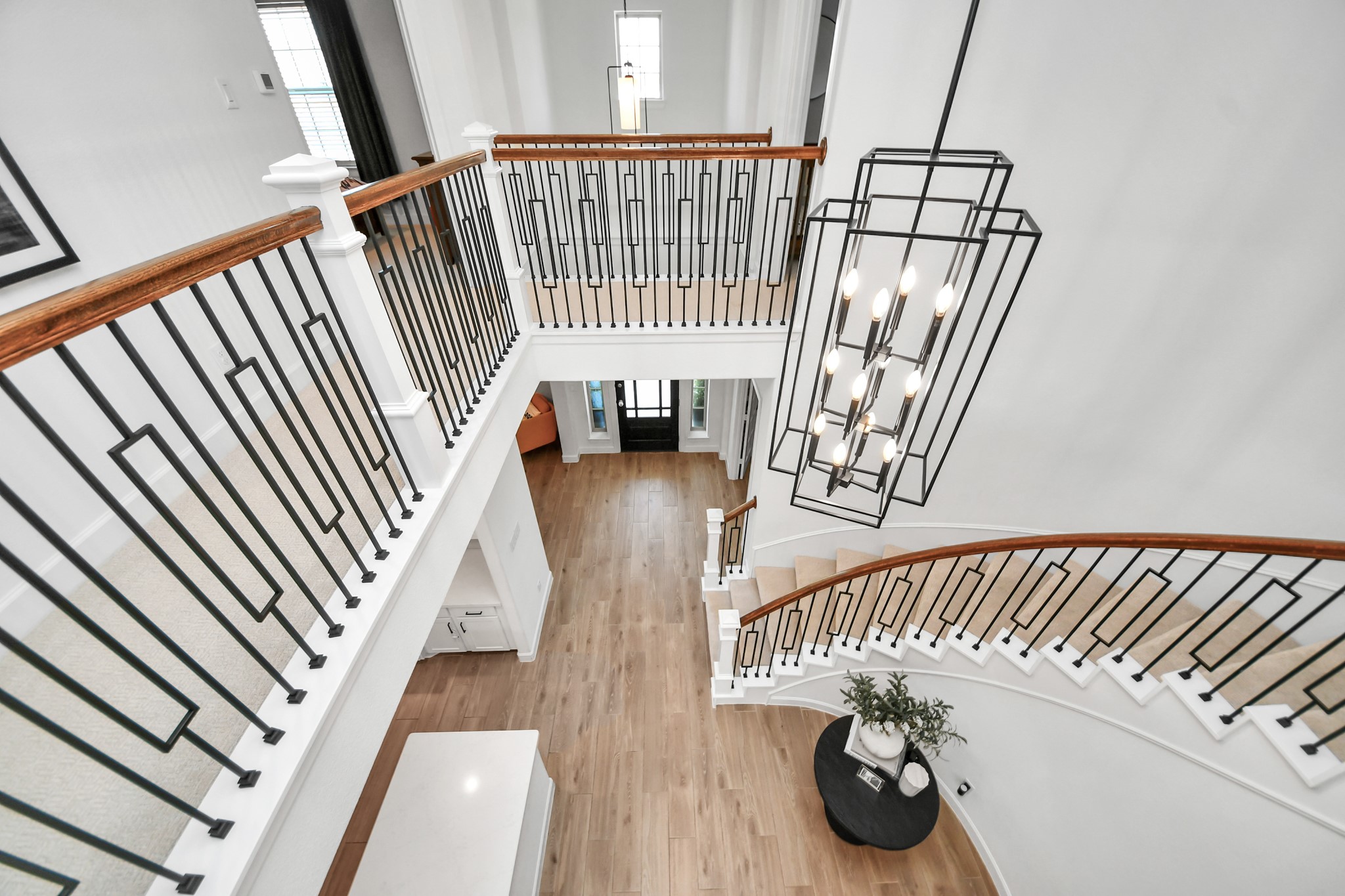 A stunning curved staircase with elegant iron railings and a striking modern chandelier highlights this foyer, offering a grand entrance with beautiful wood flooring.