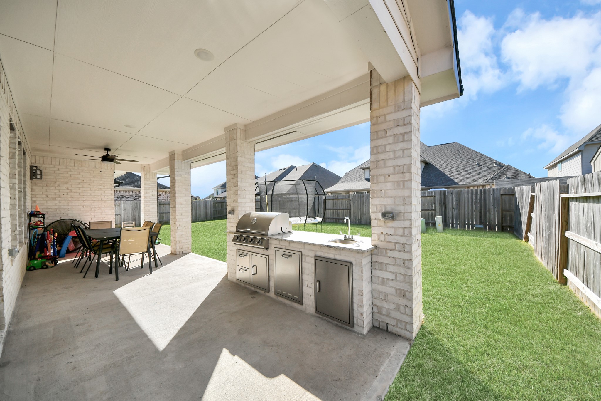 Spacious covered patio with an outdoor kitchen and dining area, perfect for entertaining and enjoying the fenced backyard.